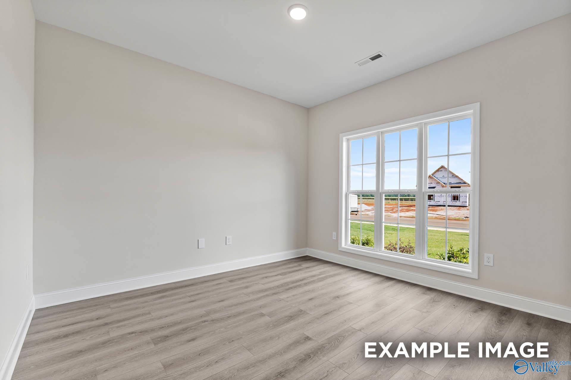 Bright secondary bedroom with beige walls, hardwood floors, and large window overlooking green lawn in Davidson Homes The Finleigh, Huntsville