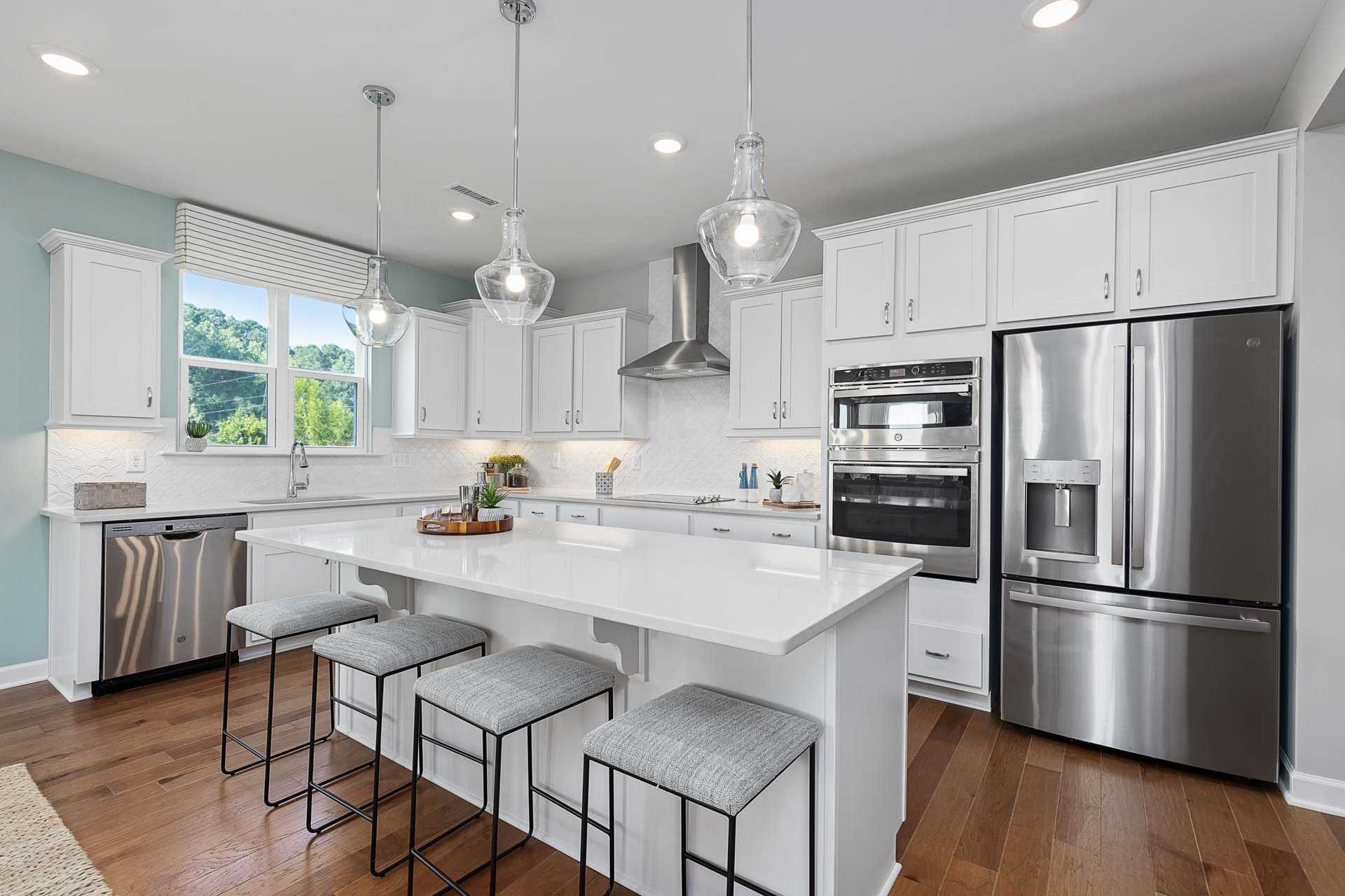 Modern kitchen in Highland Forest Fuquay-Varina NC by Davidson Homes with white island, stainless appliances, pendant lights, hardwood floors