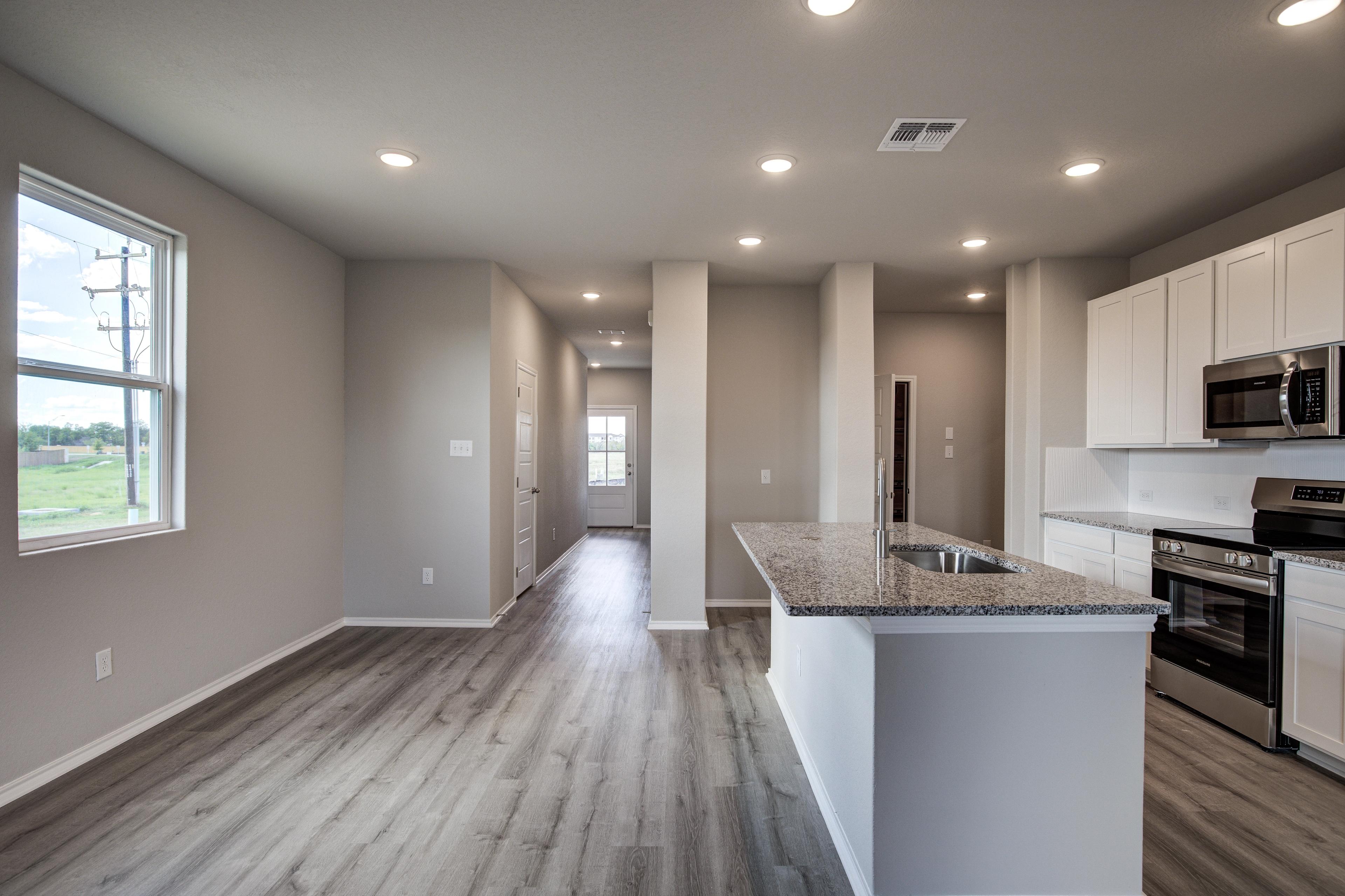 Open-concept kitchen and hallway in The Blanco C home by Davidson Homes, with white cabinets, granite island, stainless appliances, and hardwood floors