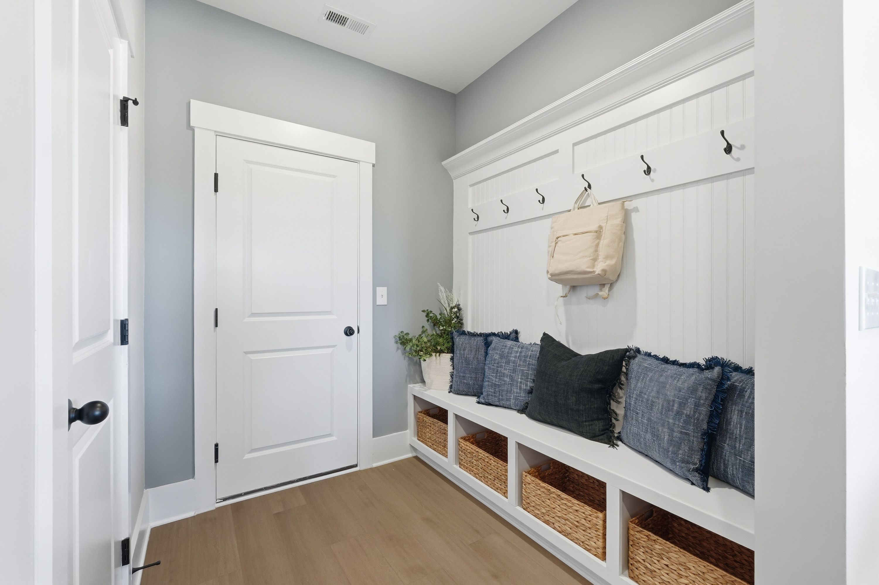 Cozy mudroom entryway at Berry Cove in New Market, Alabama with built-in bench, coat hooks, pillows, and wicker baskets on hardwood floors