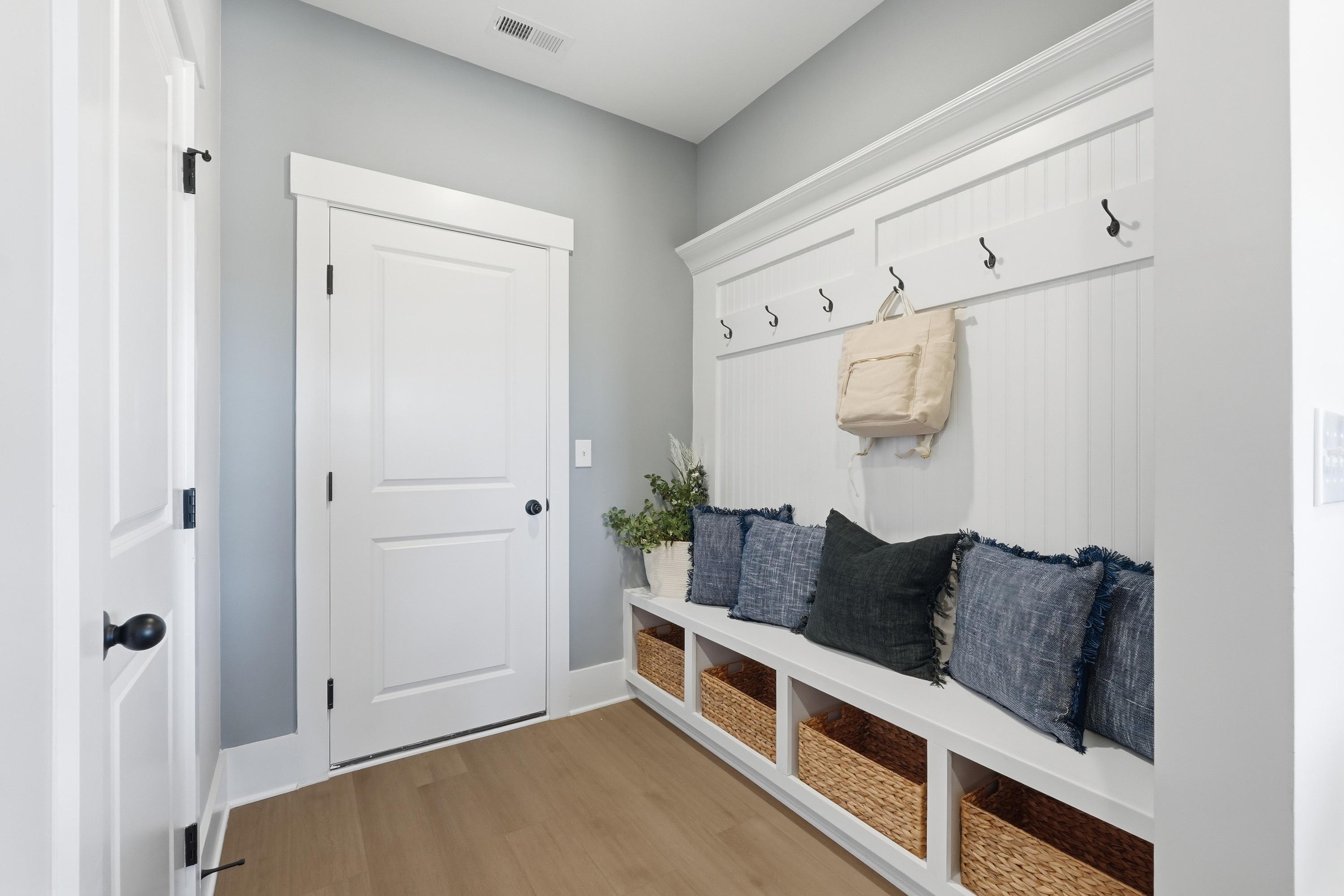 Cozy mudroom entryway at Berry Cove in New Market, Alabama with built-in bench, coat hooks, pillows, and wicker baskets on hardwood floors