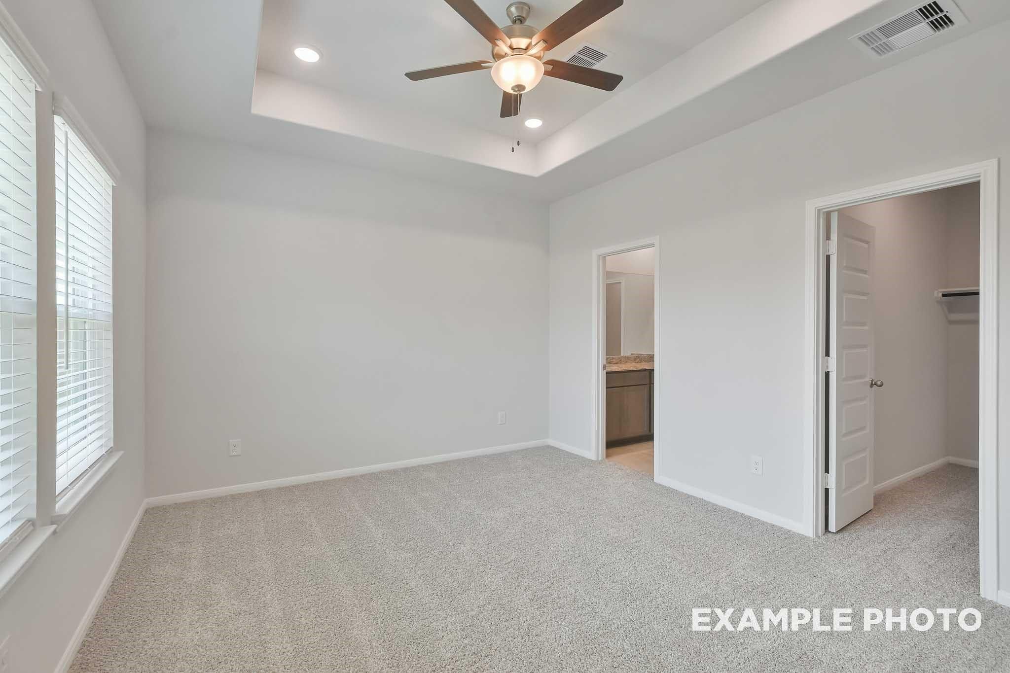 Bright master bedroom with ceiling fan, carpeted floors, and walk-in closet access in Davidson Homes The Frio F, Conroe, Texas