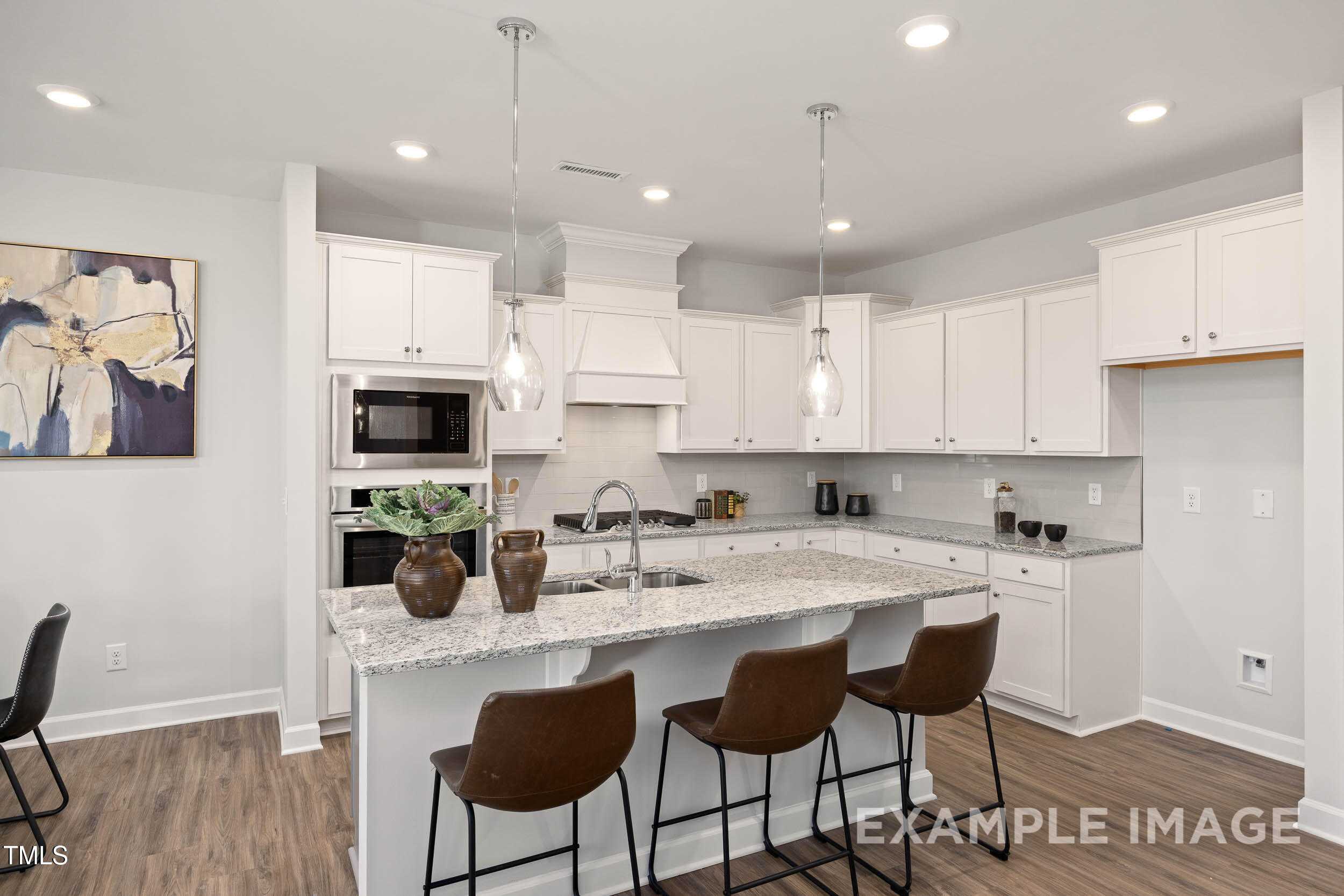 Modern kitchen featuring white shaker cabinets, granite island with bar stools, and pendant lights in Davidson Homes The Graham, Fuquay-Varina, NC