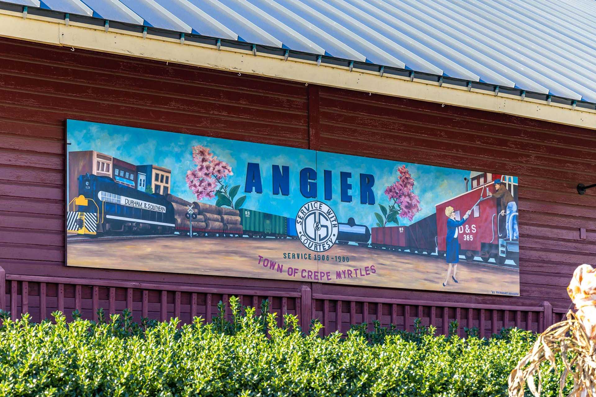 Vibrant train mural on red barn wall at Tobacco Road in Angier, North Carolina with steam locomotive and crape myrtle town sign