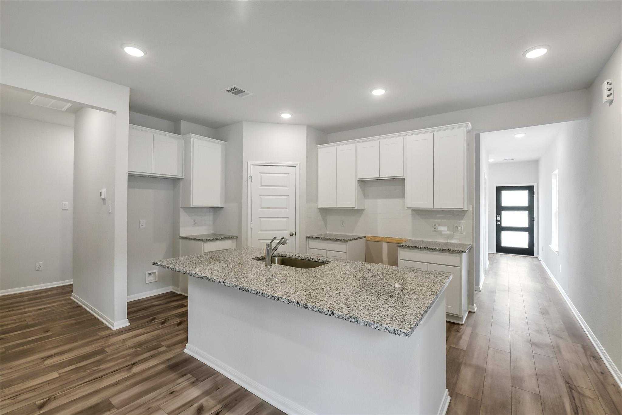Modern open-concept kitchen with white cabinets, granite island sink, and wood floors in Davidson Homes The Sabine E, Conroe TX