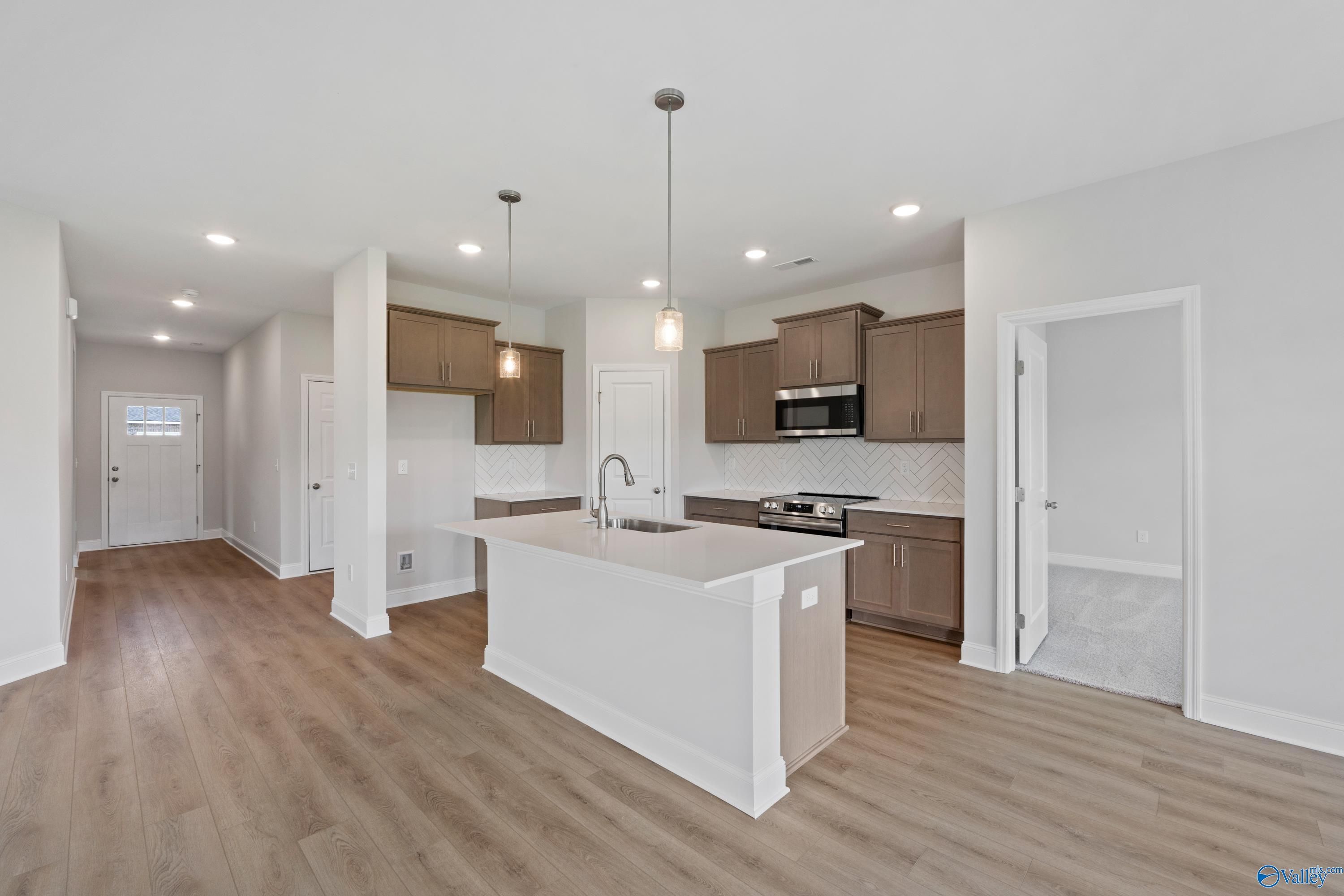 Modern open-concept kitchen featuring white island, brown cabinets, stainless appliances in Davidson Homes The Franklin C, Harvest, AL