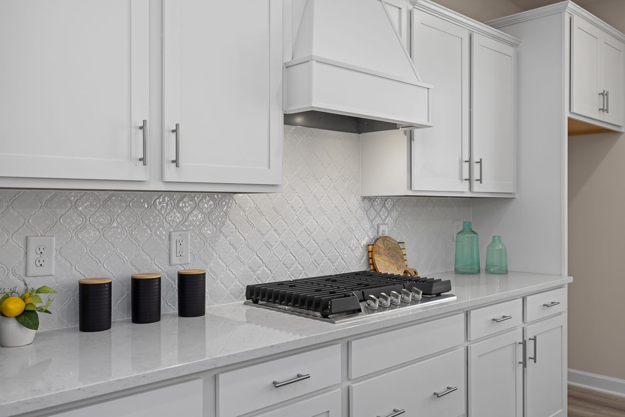 Modern kitchen in The Chestnut featuring white shaker cabinets, quartz countertops, and decorative arabesque backsplash.