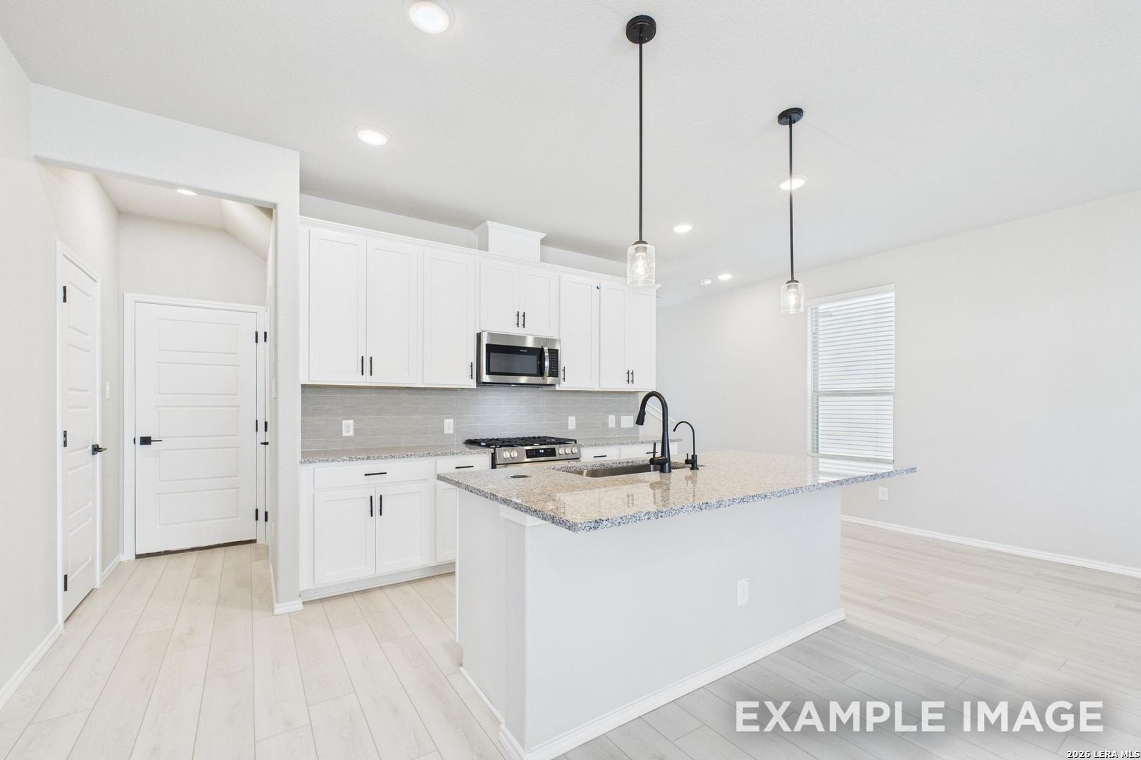 Modern kitchen with white cabinets, granite island, and pendant lighting in Davidson Homes The Charlotte B, San Antonio.