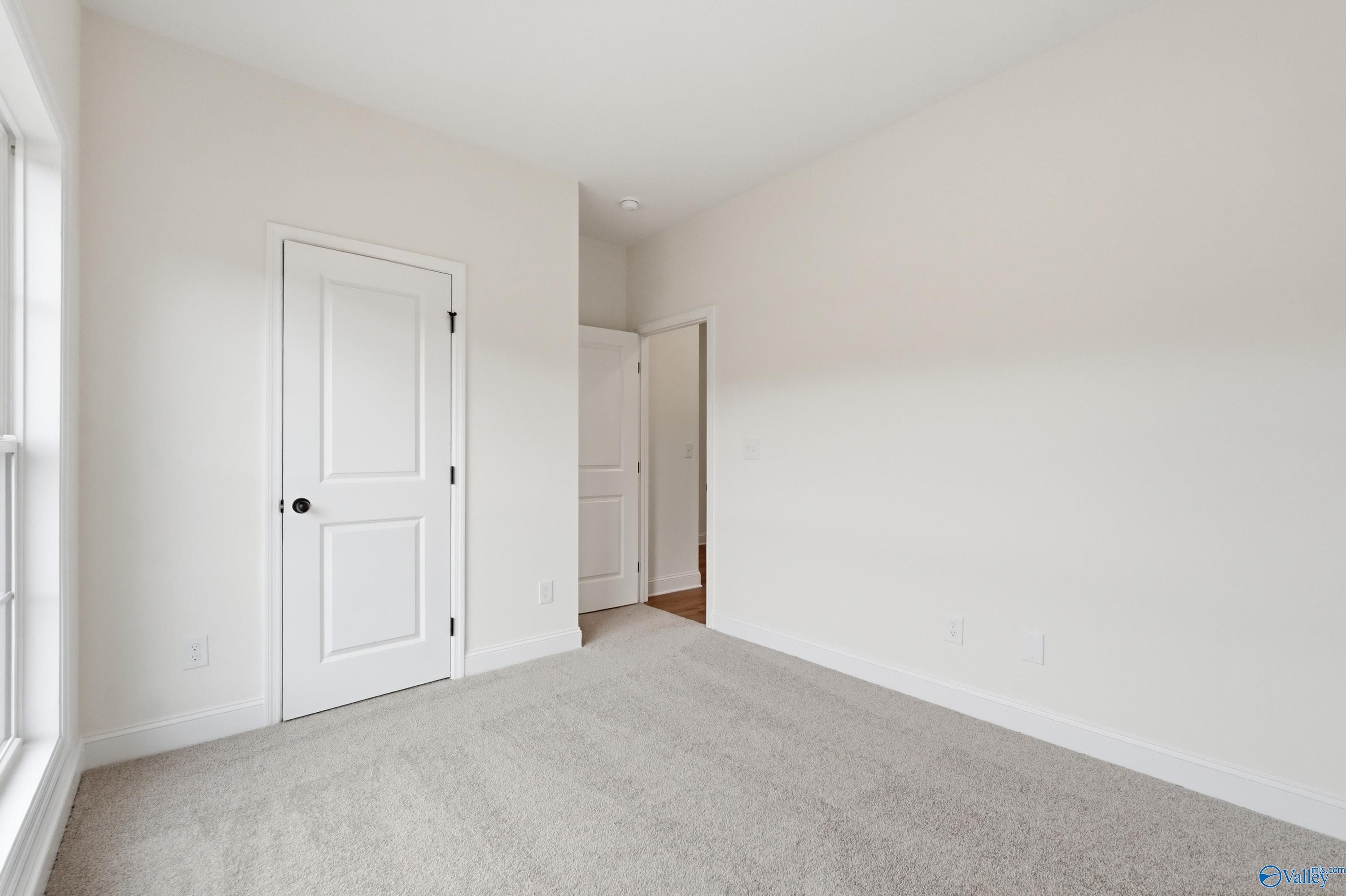Empty secondary bedroom with white walls, beige carpet, large window, and double doors in Davidson Homes The Asheville C, Arab, Alabama