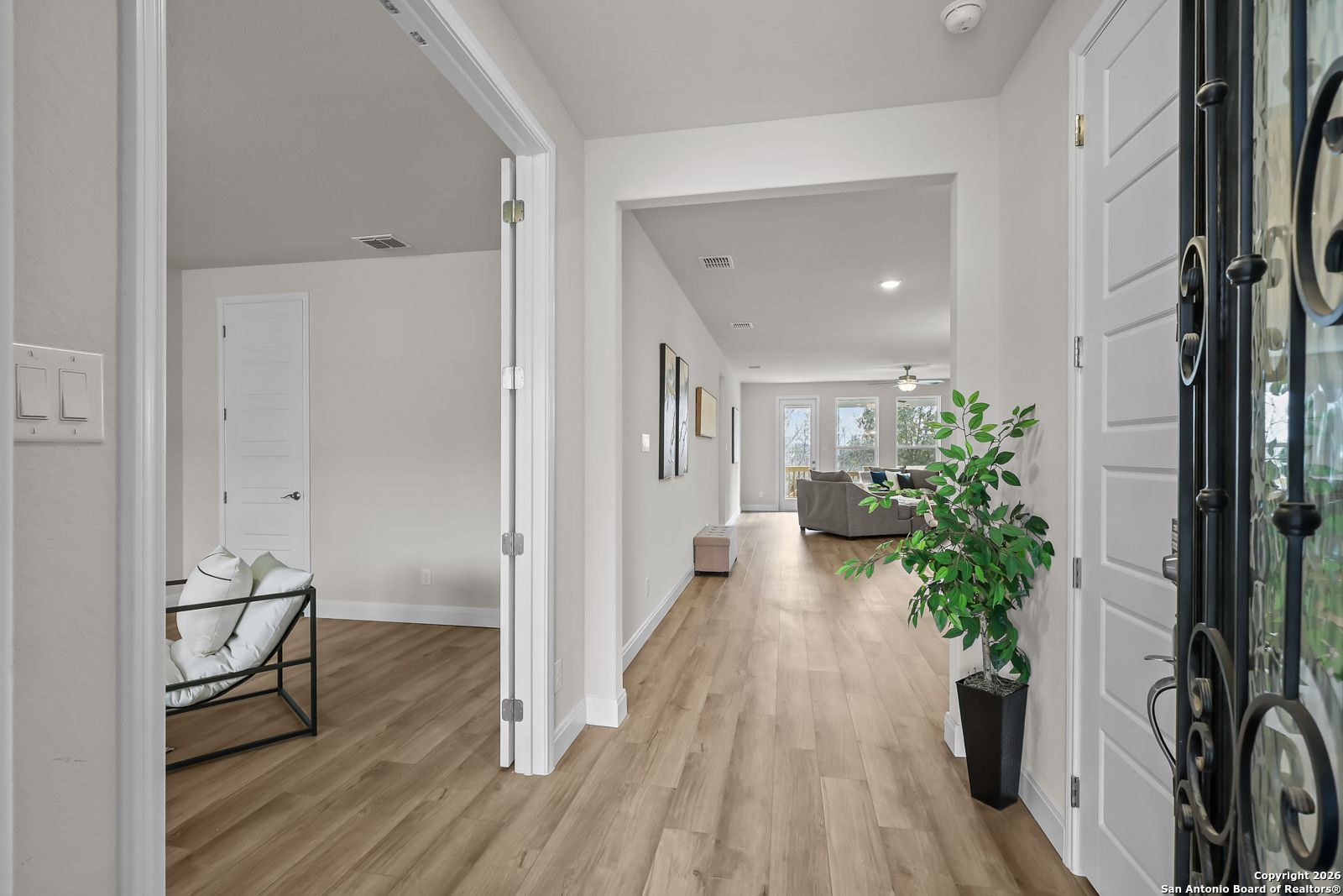 Bright entryway with wood floors, open doors to living room, potted plant, and gray sofa in The Lanier H, Davidson Homes, Ladera, San Antonio