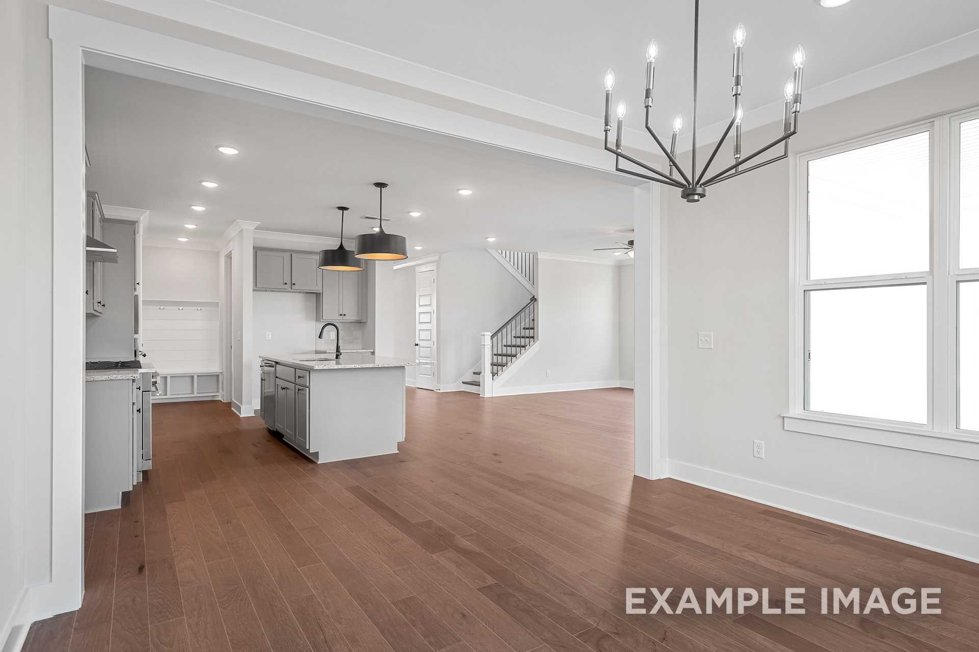 Spacious open-concept kitchen in The Hathaway featuring white cabinets, large island sink, pendant lights, hardwood floors, and adjacent staircase