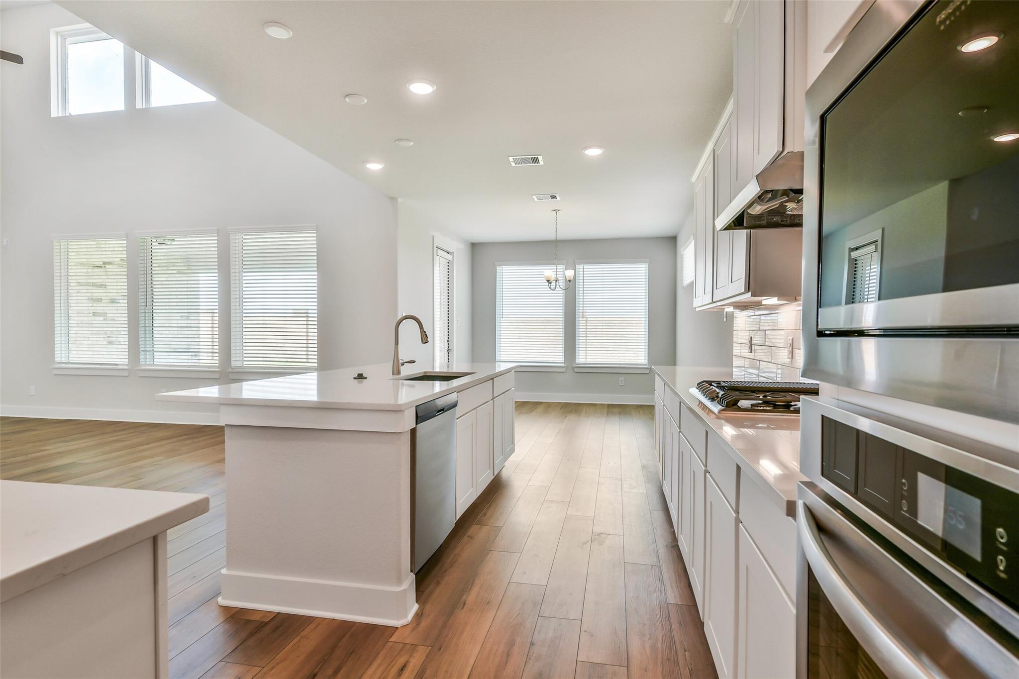 Modern kitchen with white shaker cabinets, large island sink, stainless steel range and oven in Davidson Homes The Victoria A, Lago Mar Texas