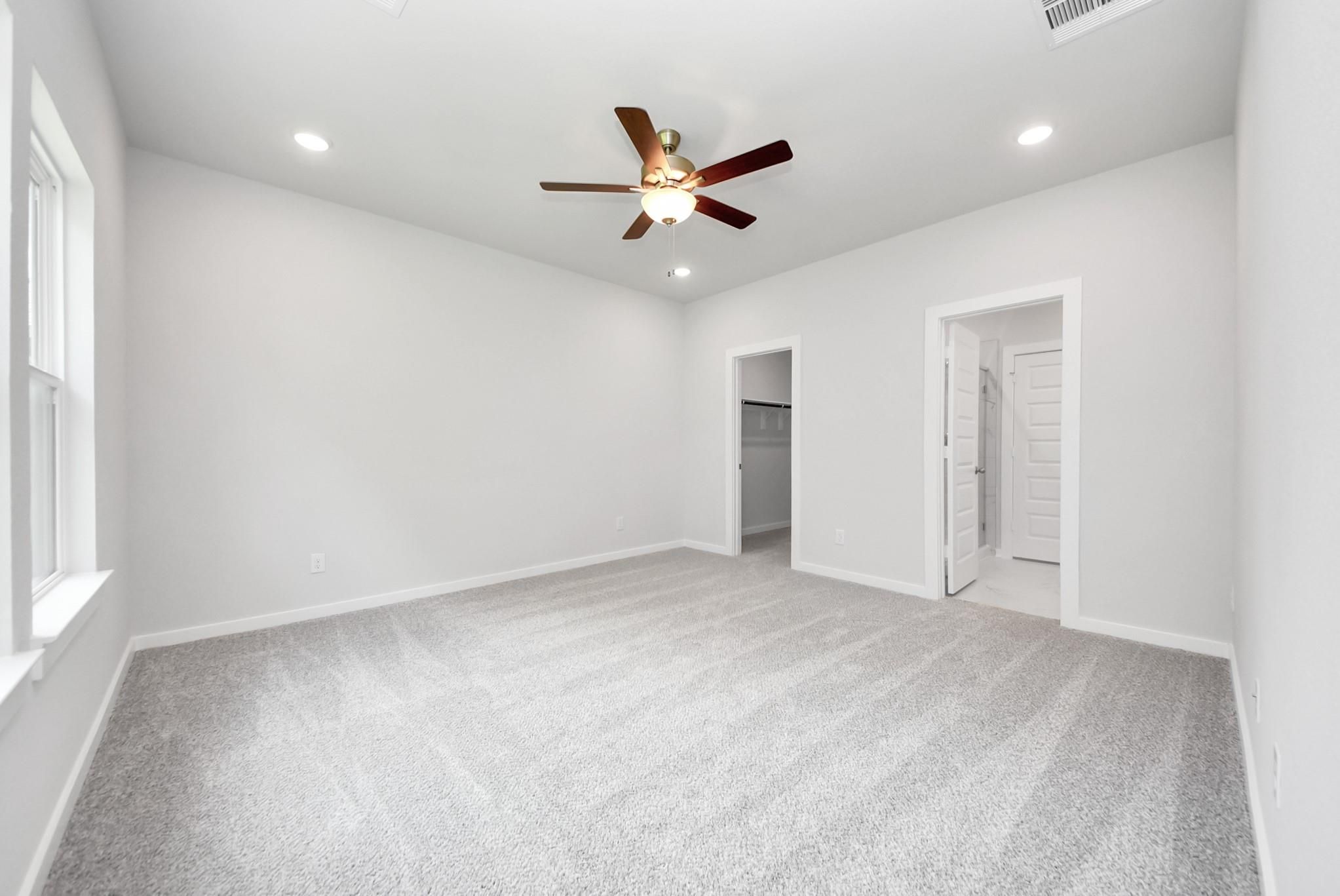 Spacious bedroom with carpet, ceiling fan, and walk-in closet in The Sabine E floor plan at Windmill Estates, Magnolia.