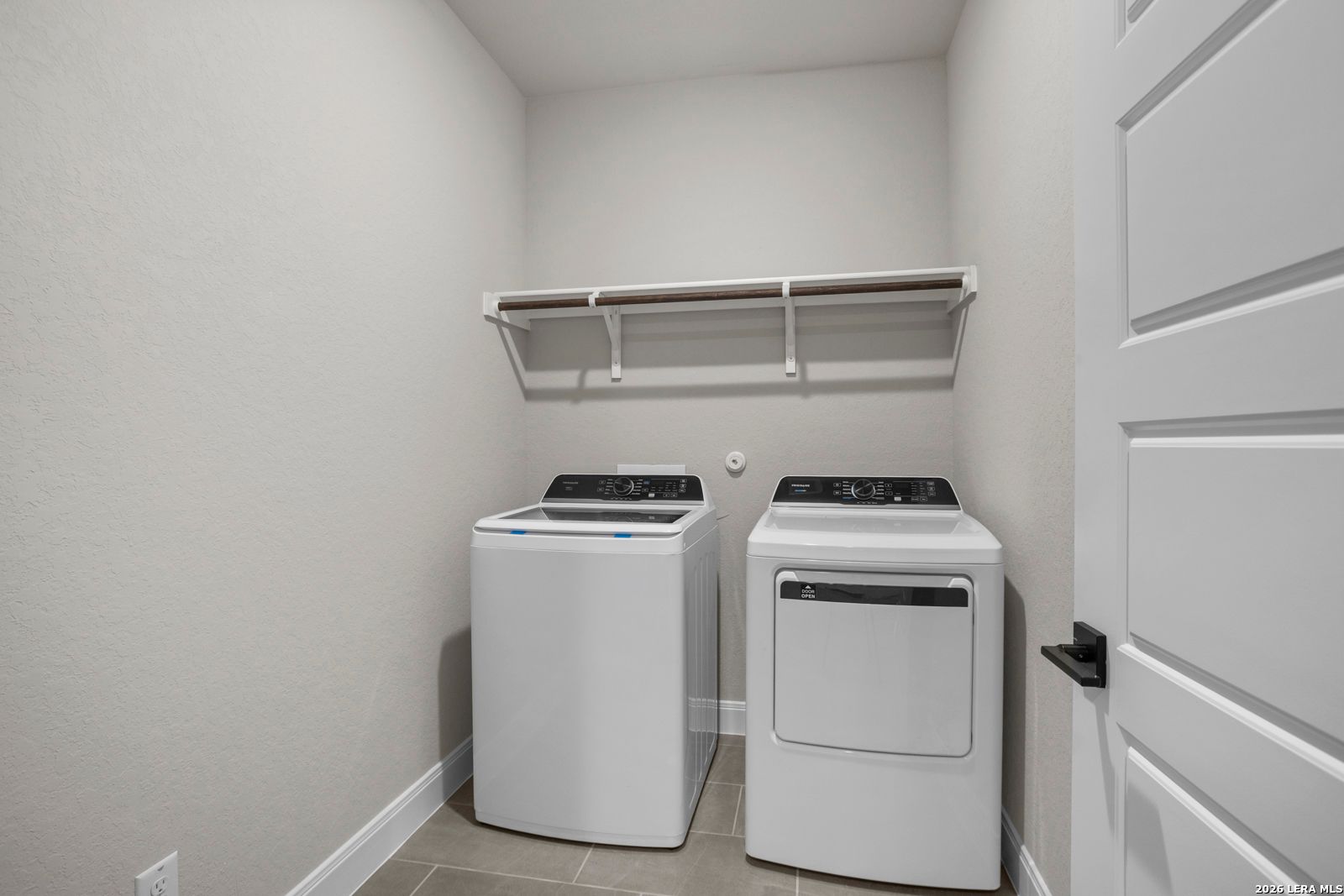 Laundry room with white washer and dryer, shelving, and tile flooring in The Jennings G floor plan at Ladera, San Antonio.