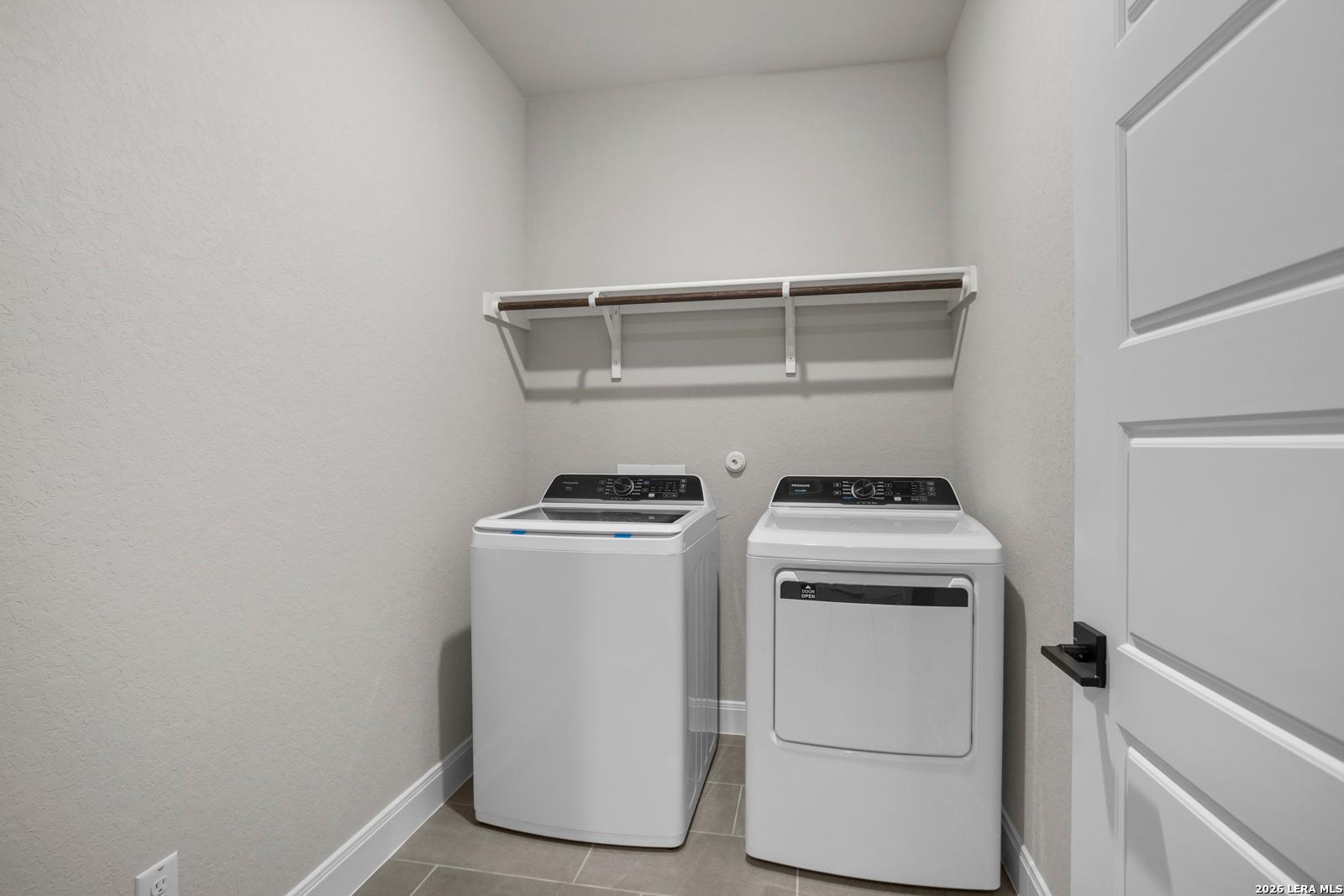 Laundry room with white washer and dryer, shelving, and tile flooring in The Jennings G floor plan at Ladera, San Antonio.