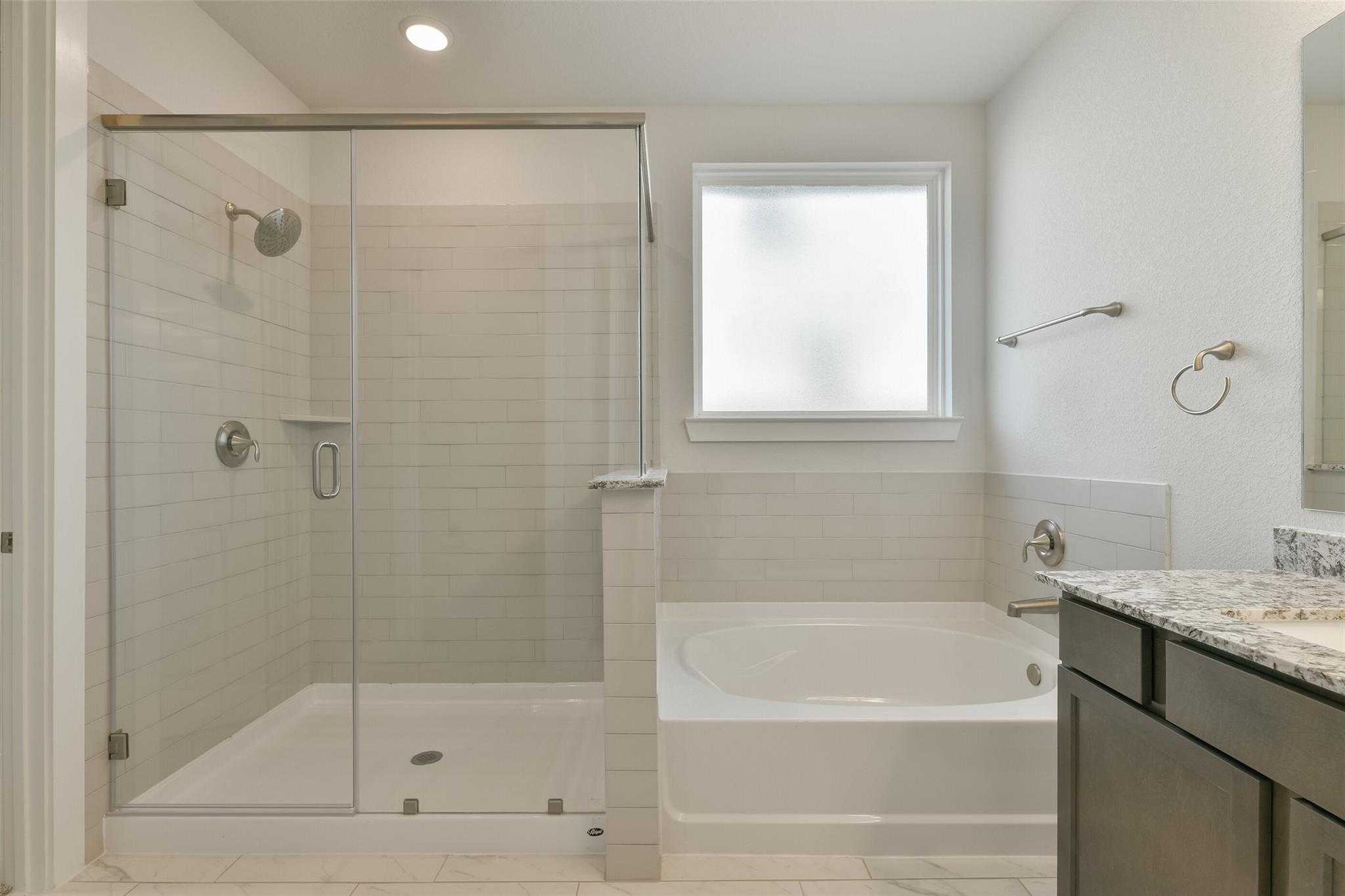 Elegant master bathroom with frameless glass shower, soaking tub, and granite double vanity in Davidson Homes The Edward A, Lago Mar, Texas City