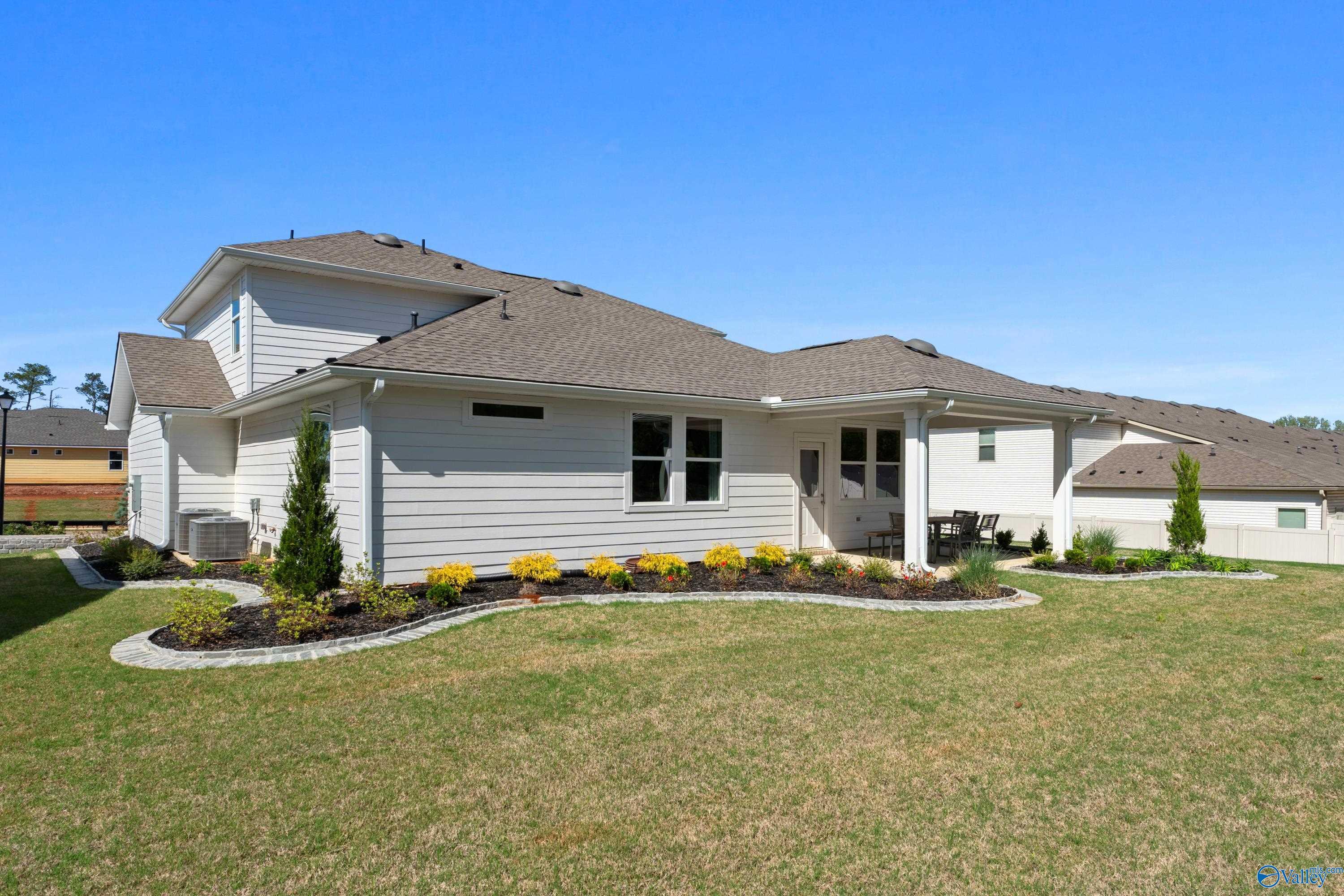 Two-story white Davidson Homes The Stella with covered patio, yellow flower beds, shrubs, and green lawn in Evergreen Mill, Madison AL