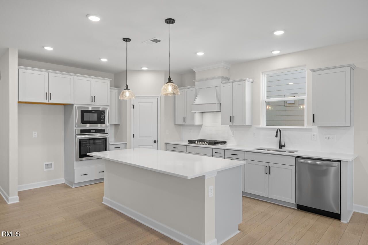Bright modern kitchen with white cabinetry, quartz island, and stainless appliances in Davidson Homes Ashport M, Wendell Ridge NC