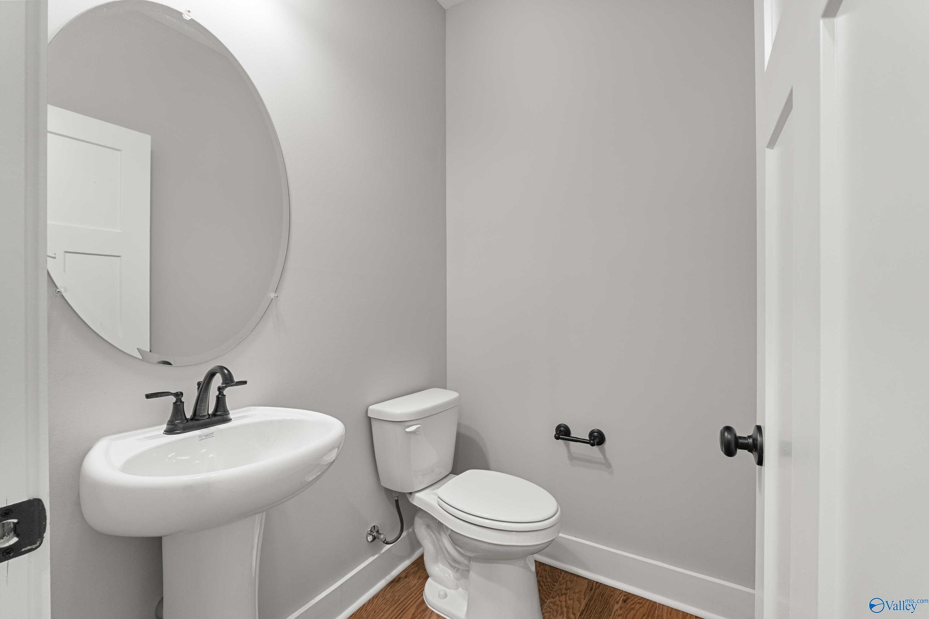 Modern powder room with white pedestal sink, round mirror, toilet, and gray walls in Davidson Homes The Arcadia, Huntsville, Alabama