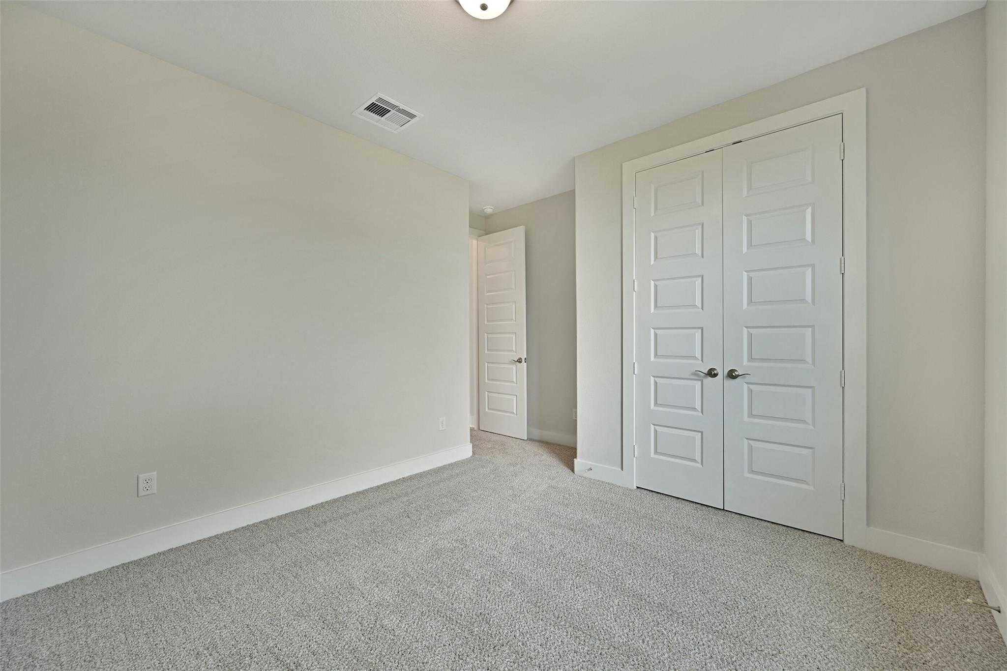 Spacious secondary bedroom with double closet doors, beige walls, and carpet in Davidson Homes The Edward A, Lago Mar, Texas City