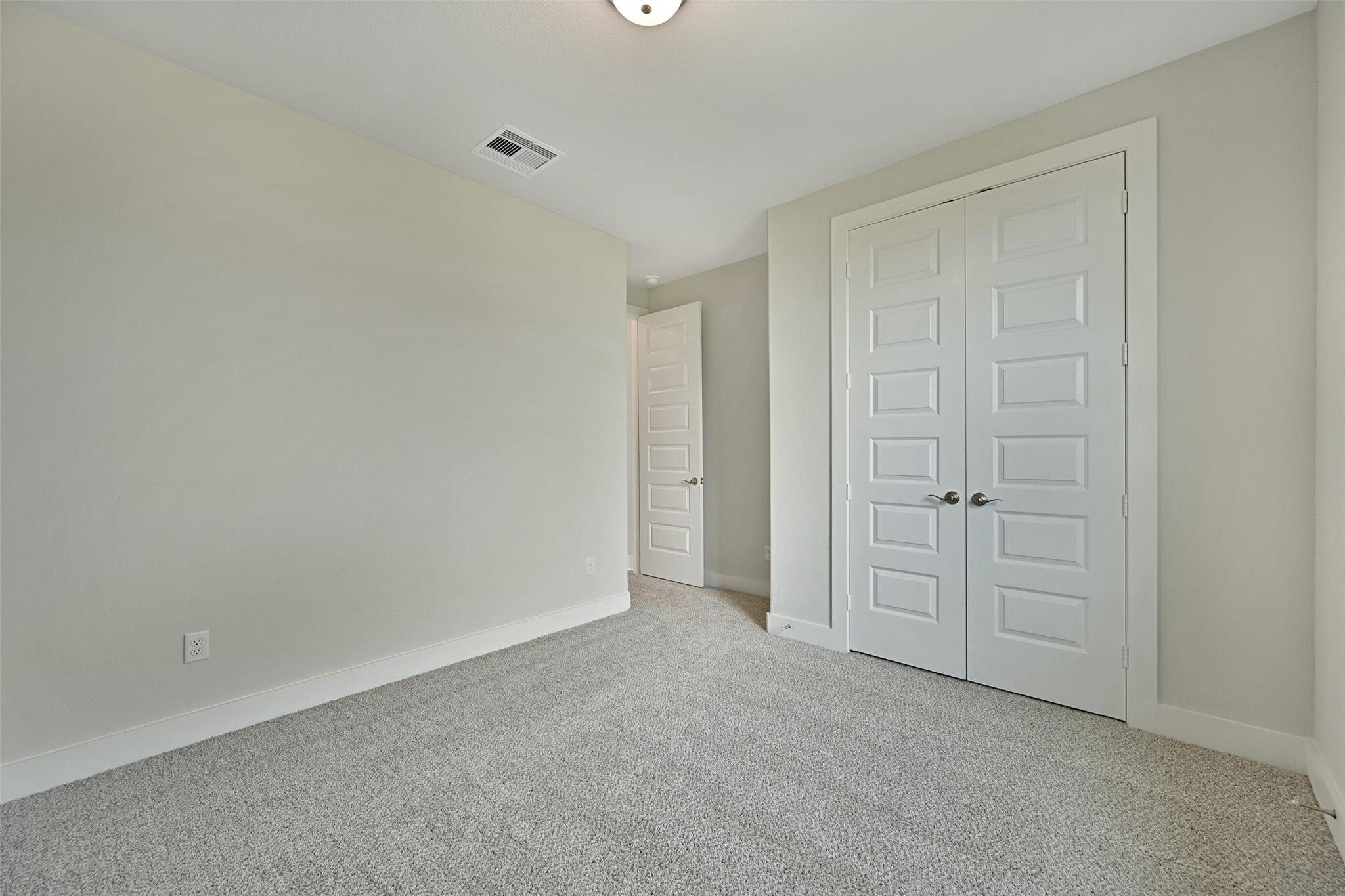Spacious secondary bedroom with double closet doors, beige walls, and carpet in Davidson Homes The Edward A, Lago Mar, Texas City