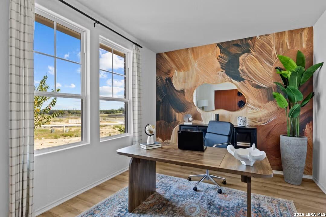 Modern home office with wooden desk, abstract earthy mural, potted plants, and scenic windows in Davidson Homes The Douglas C, Converse, Texas