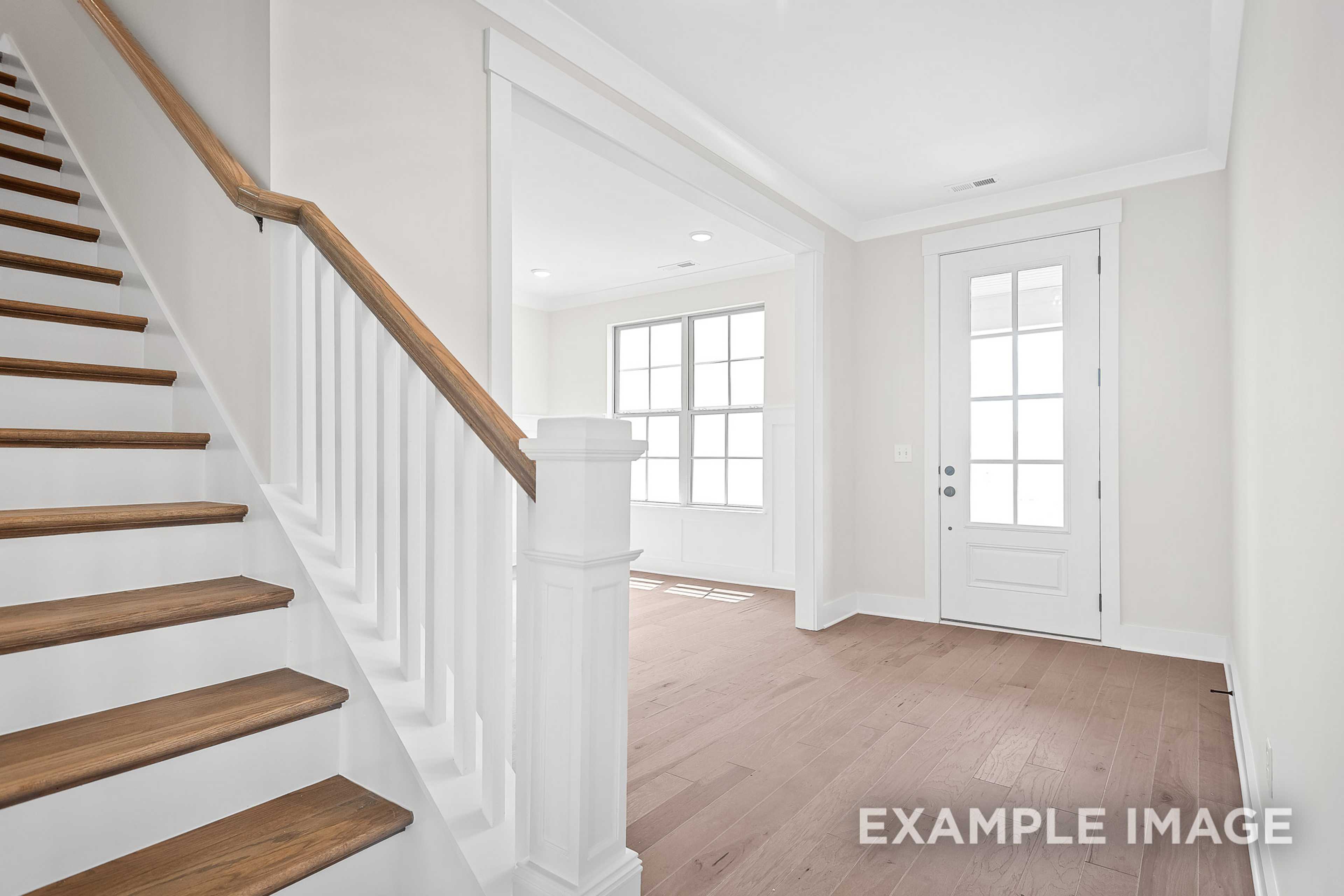 Spacious foyer with oak staircase, white railings, large windows, and hardwood floors in The Hawkins 2-story home
