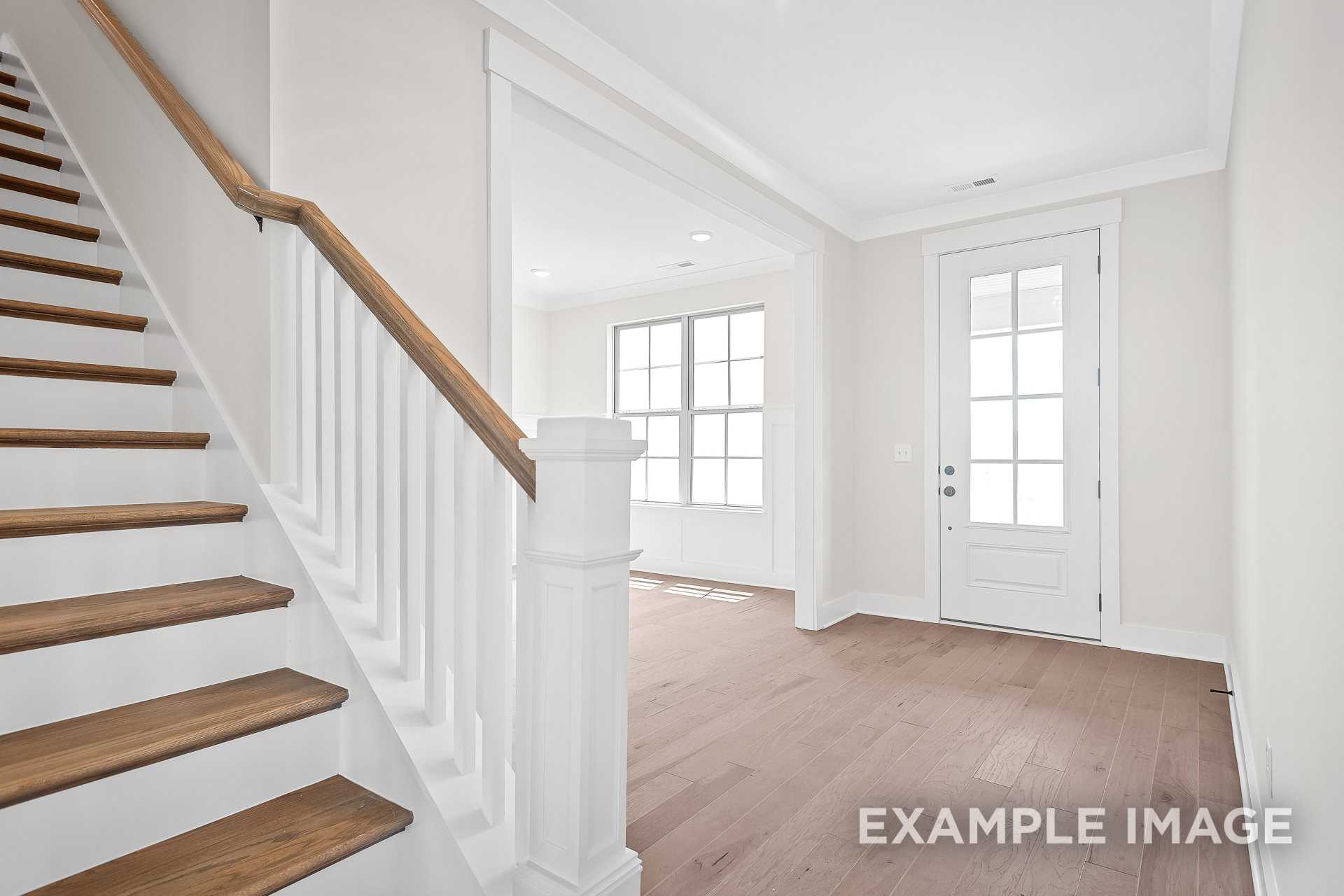 Spacious foyer with oak staircase, white railings, large windows, and hardwood floors in The Hawkins 2-story home