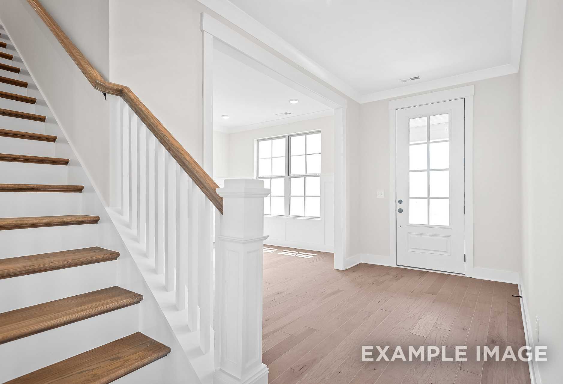 Spacious foyer with oak staircase, white railings, large windows, and hardwood floors in The Hawkins 2-story home