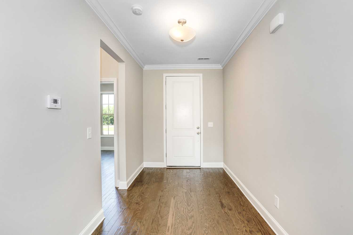 Spacious entry hallway in The Montgomery home with oak hardwood floors, beige walls, white door, and open archway