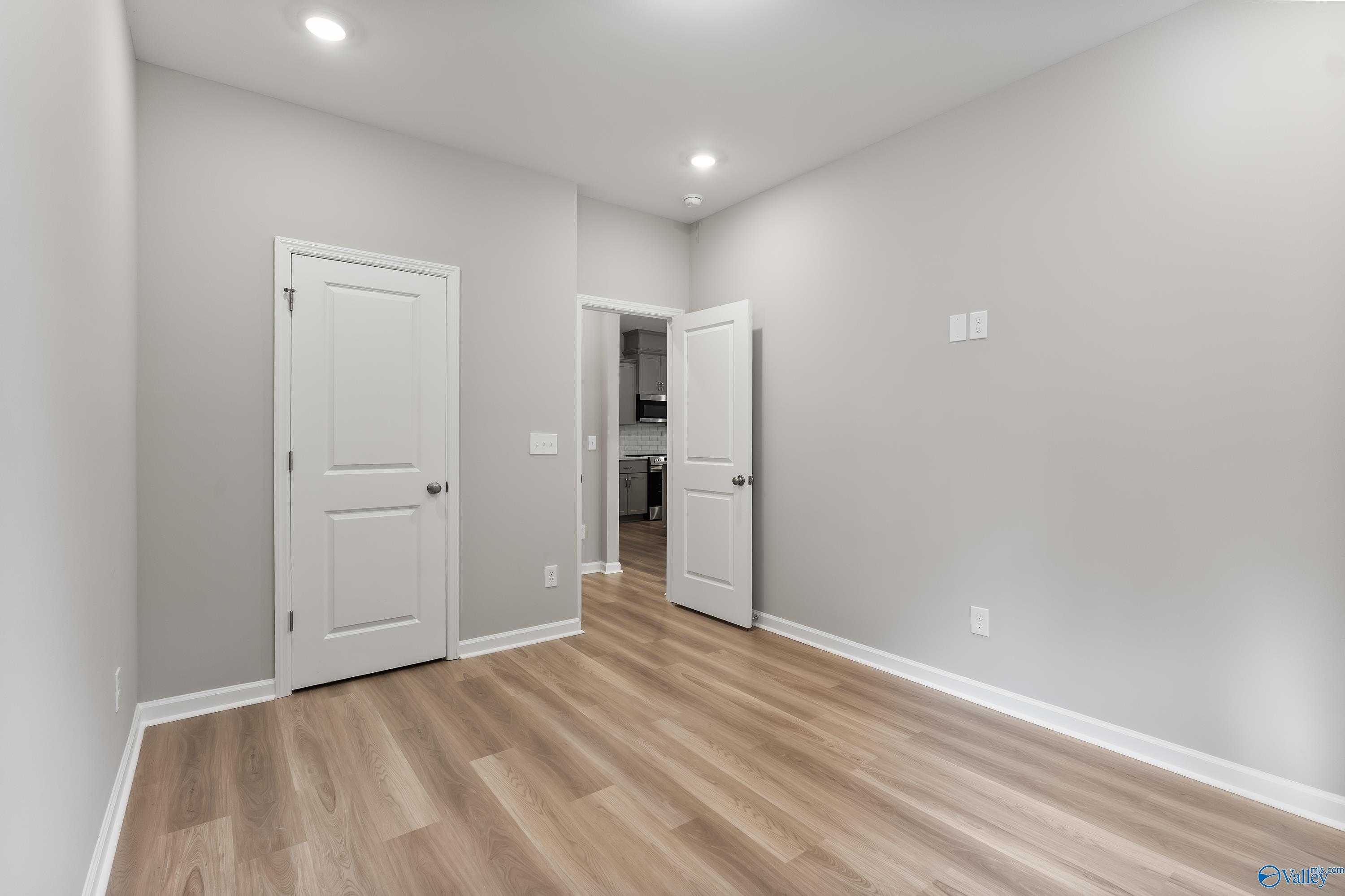 Spacious secondary bedroom with gray walls, luxury vinyl plank flooring, and open door to bath in Evermore Homes The Grace, Madison AL