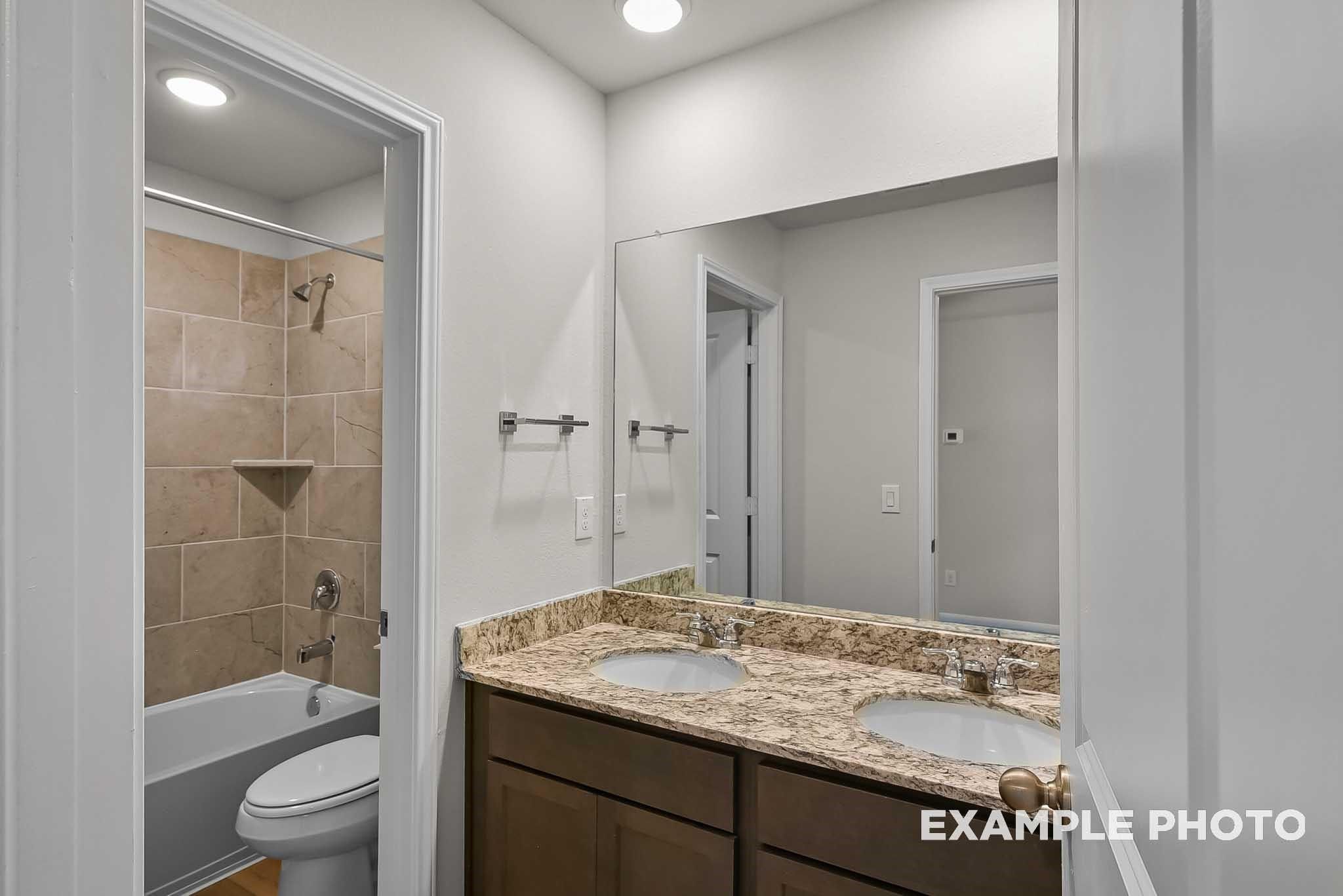 Double vanity bathroom with granite countertops and tiled shower-tub combo in The Blanco F home, Spring Branch Crossing.