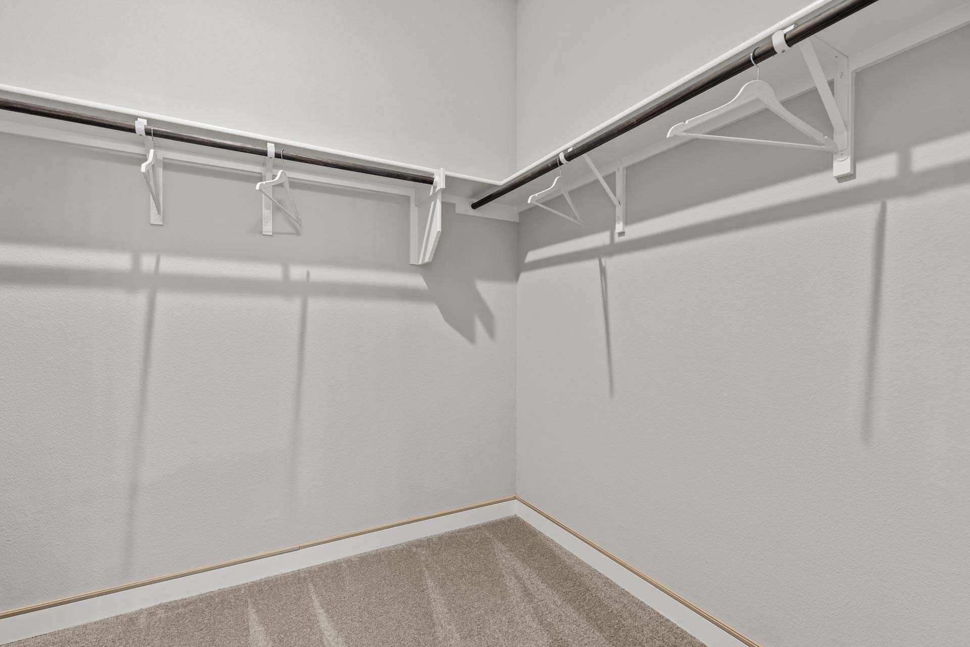 Spacious master walk-in closet in The Collin B with white walls, built-in shelves, hanging rods, and beige carpet