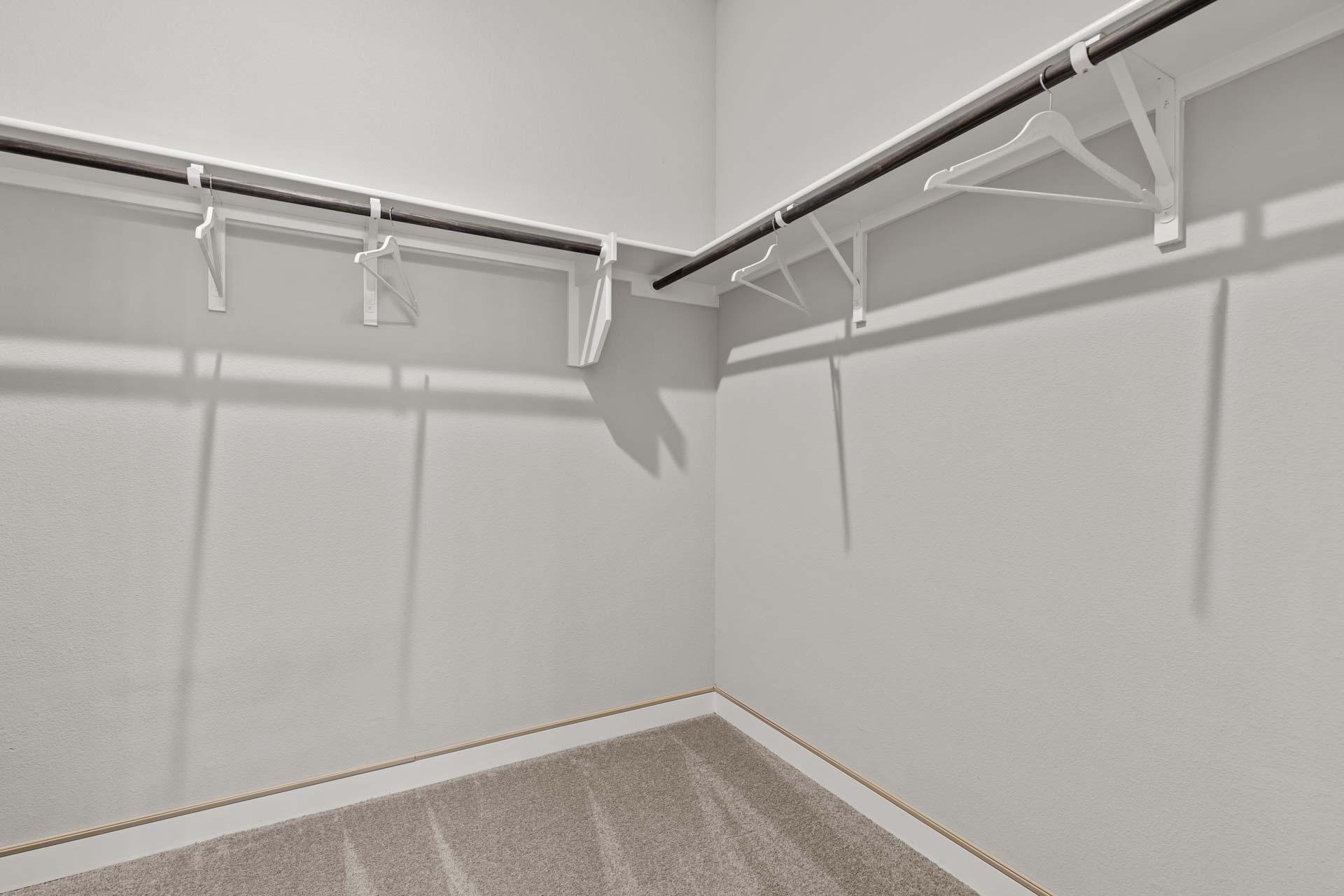 Spacious walk-in closet in The Collin A home featuring white walls, metal hanging rods, brackets, and beige carpet flooring