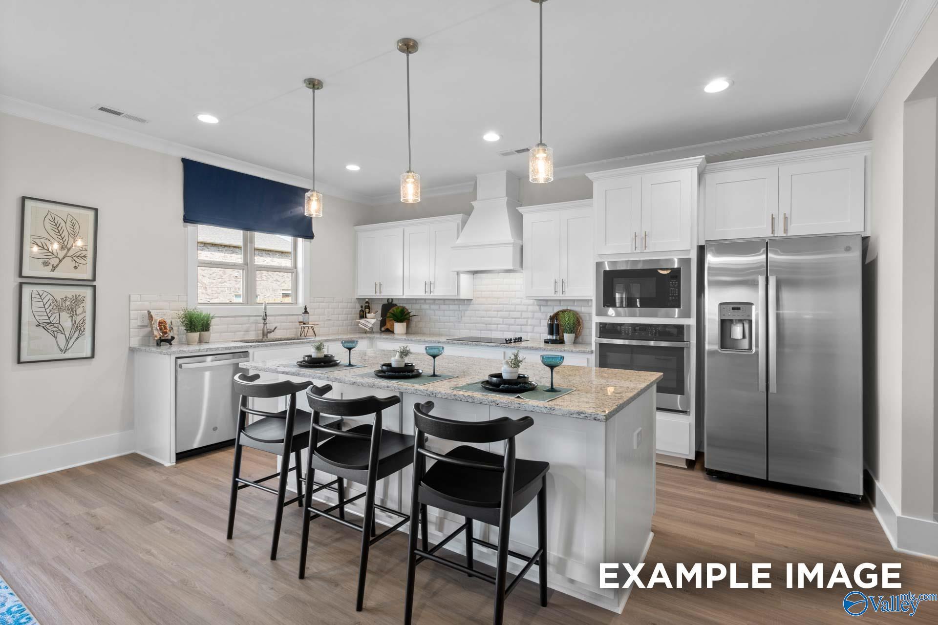 Modern kitchen with white cabinets, granite island, and stainless steel appliances in The Chelsea B at Ramsay Cove.