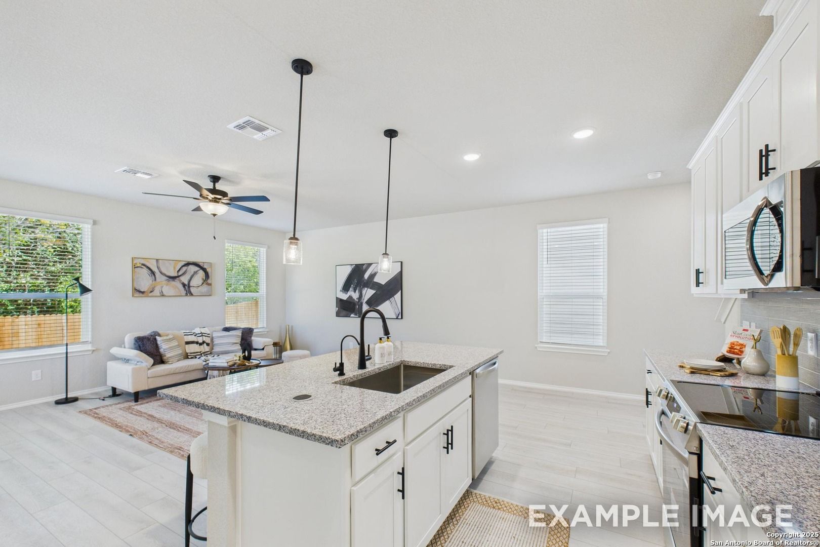 Modern open-concept kitchen and living area with quartz island, white cabinets, and pendant lights in Davidson Homes The Charlotte A, San Antonio