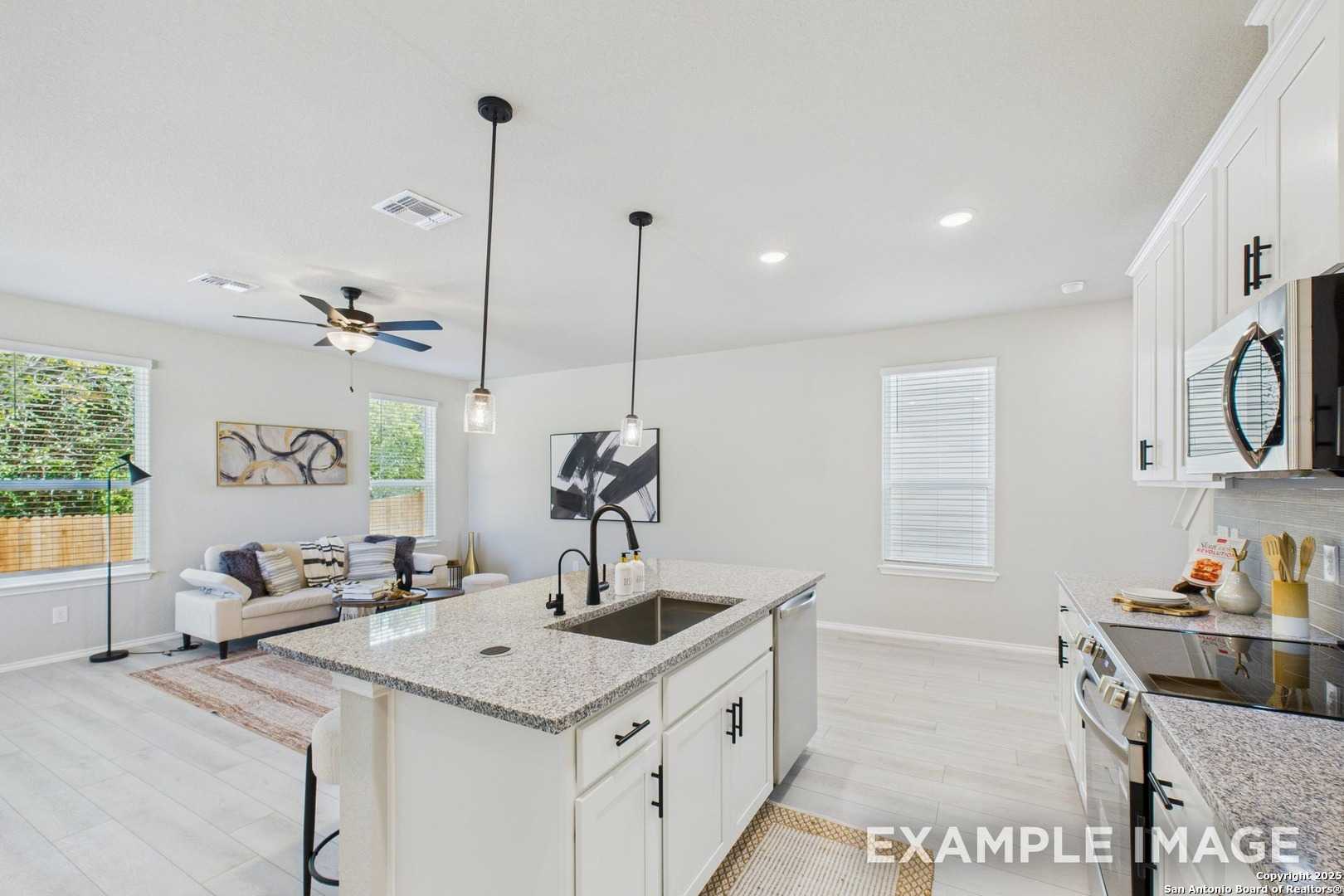 Modern open-concept kitchen and living area with quartz island, white cabinets, and pendant lights in Davidson Homes The Charlotte A, San Antonio