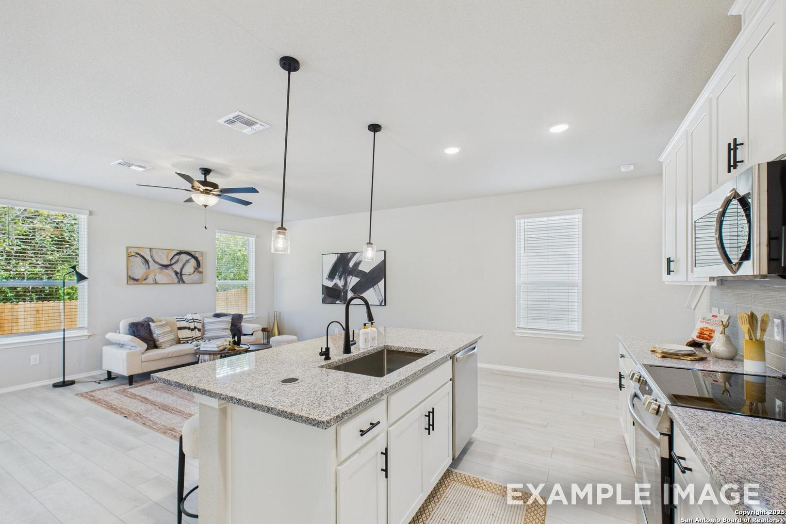 Modern open-concept kitchen with white cabinets, granite island sink, stainless appliances, and adjacent living area in Davidson Homes The Charlotte B, San Antonio