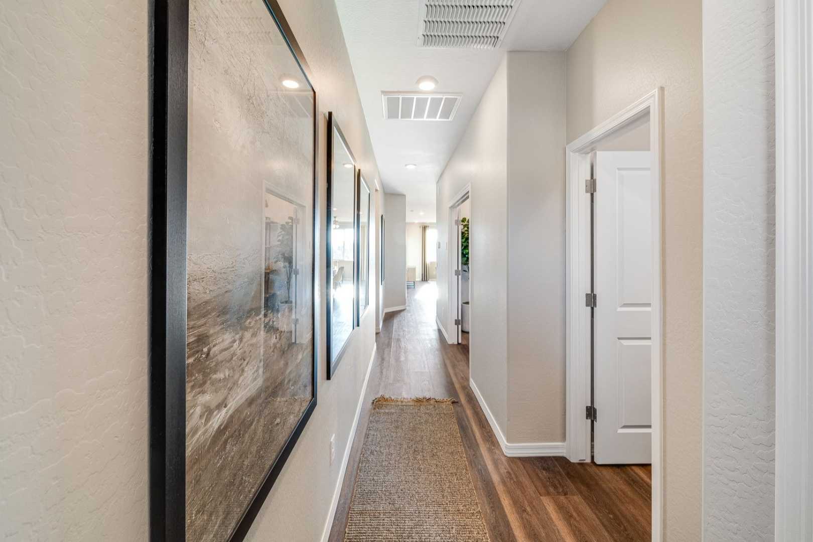 Spacious hallway interior of The Savannah C home in Prescott AZ, featuring neutral walls, hardwood floors, runner rug, and framed artwork