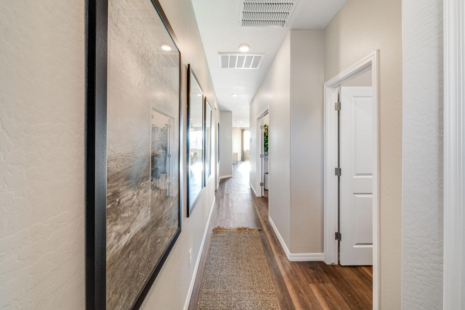 Spacious hallway in The Savannah B home featuring hardwood floors, neutral beige walls, large framed artwork, and adjacent doors
