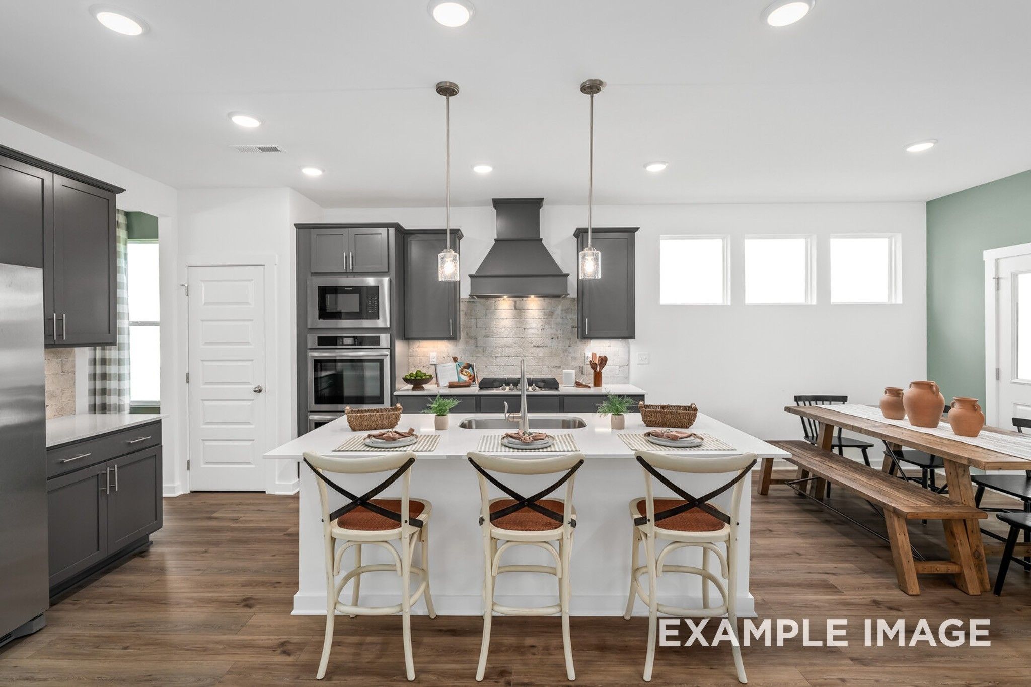 Modern open-concept kitchen with white island, dark cabinets, stainless double oven, and pendant lights in Davidson Homes The Ash A, Gallatin, TN