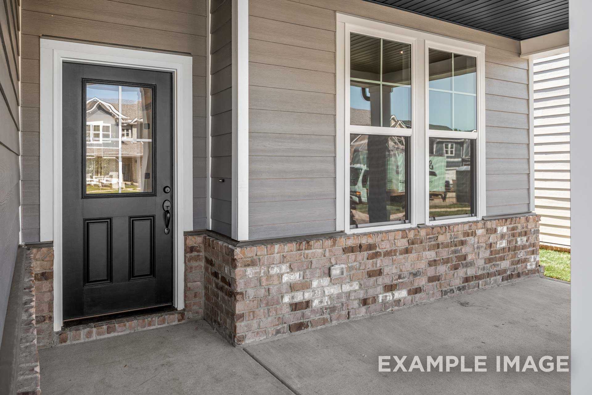 Front entrance of The Henry B home design featuring black double door, gray siding, brick base, and covered porch in Mt. Juliet
