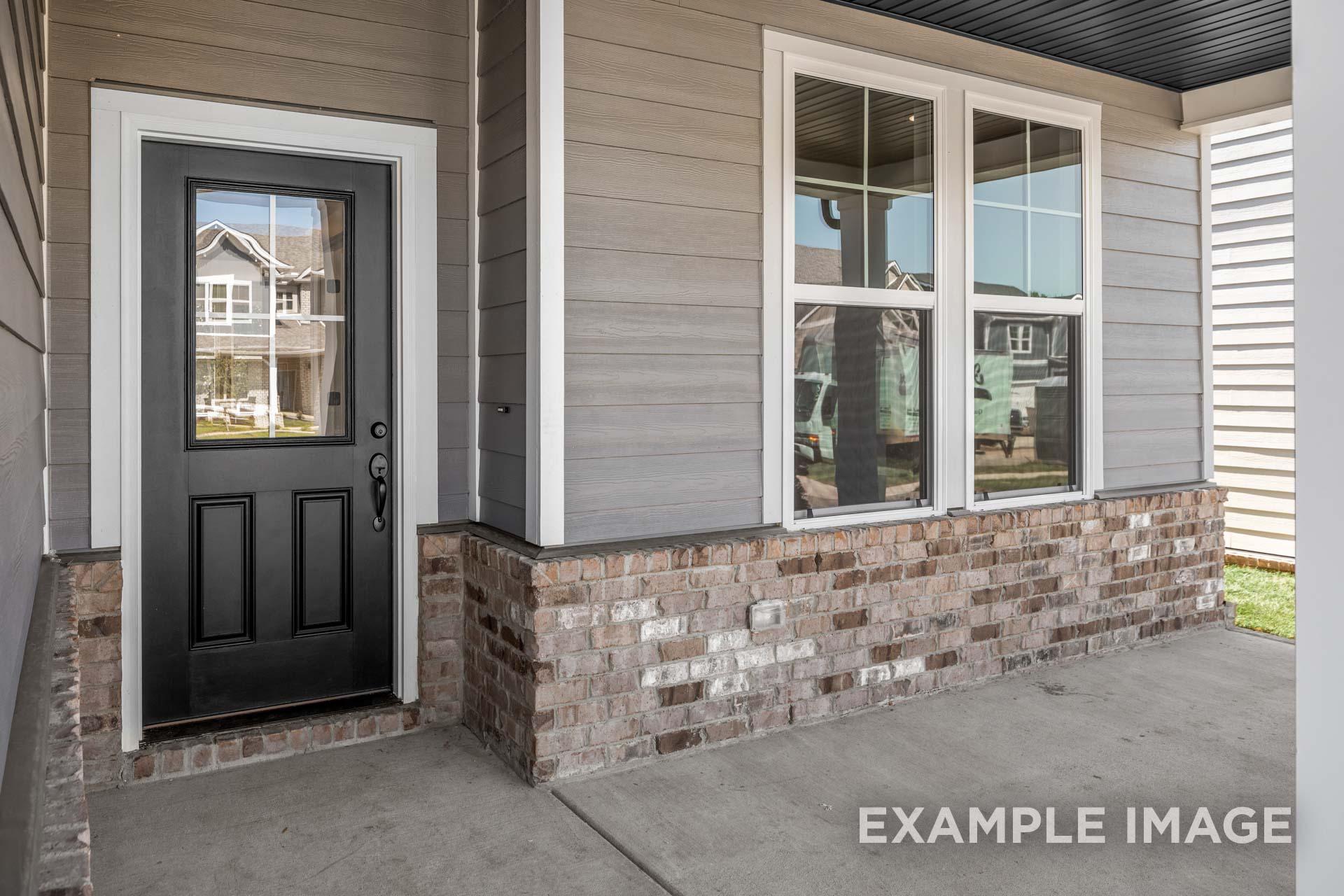 Front entrance of The Henry B home design featuring black double door, gray siding, brick base, and covered porch in Mt. Juliet