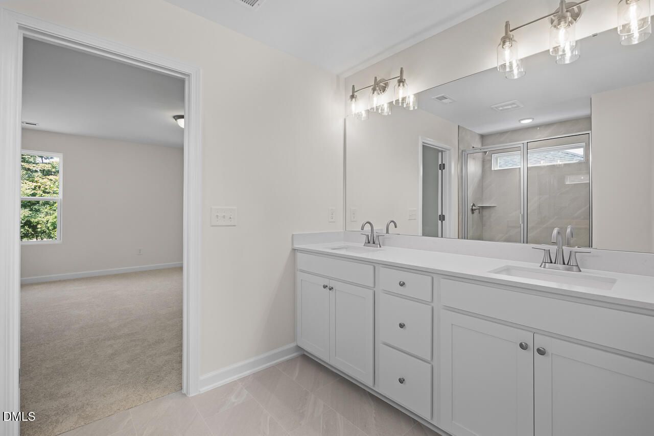 Dual vanity primary bathroom with white cabinetry and tile shower in Davidson Homes The Willow B, Zebulon, North Carolina