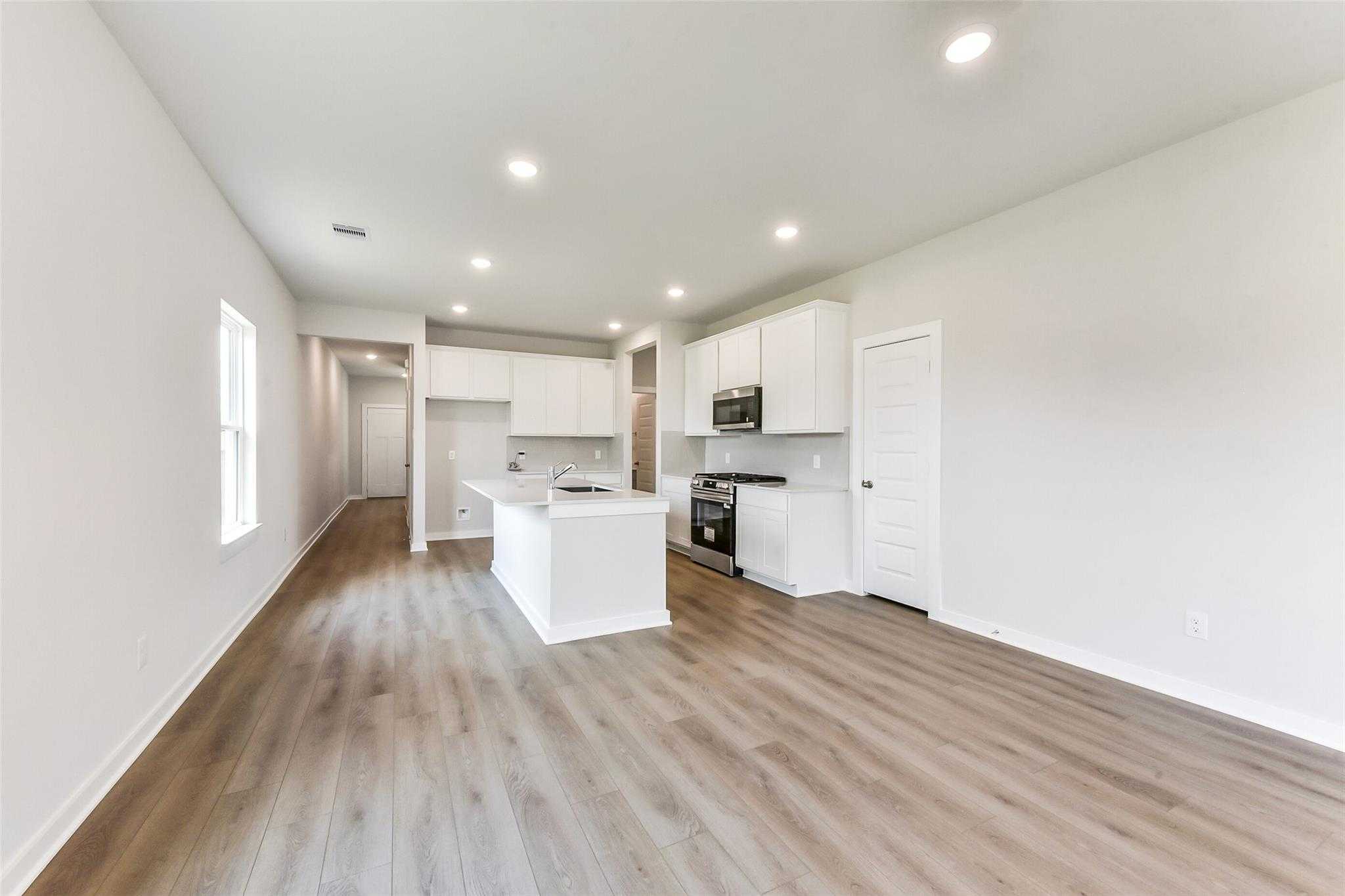 Modern open-concept kitchen with white island, stainless appliances, hardwood floors in The Frio F, Dayton, Texas