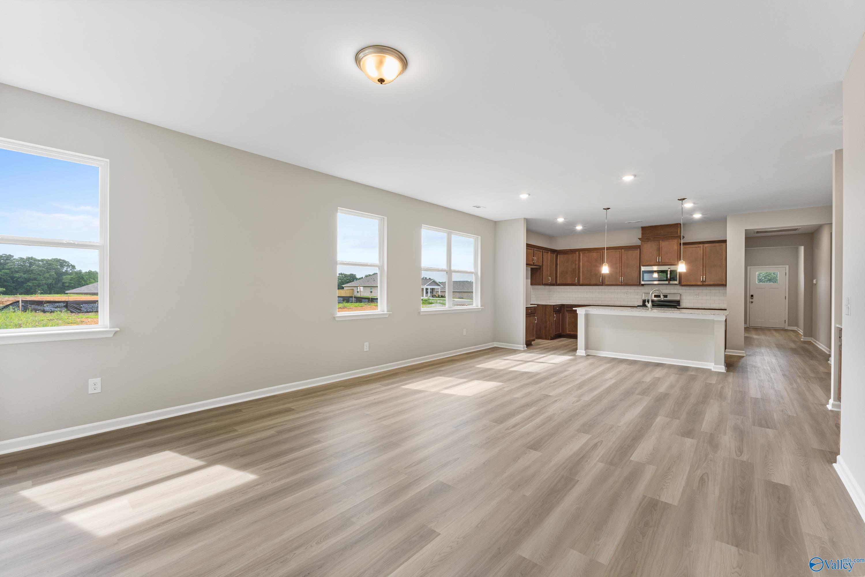 Open-concept kitchen and living area with white cabinets, island, hardwood floors, and large windows in Davidson Homes The Aurora, Fayetteville, Tennessee
