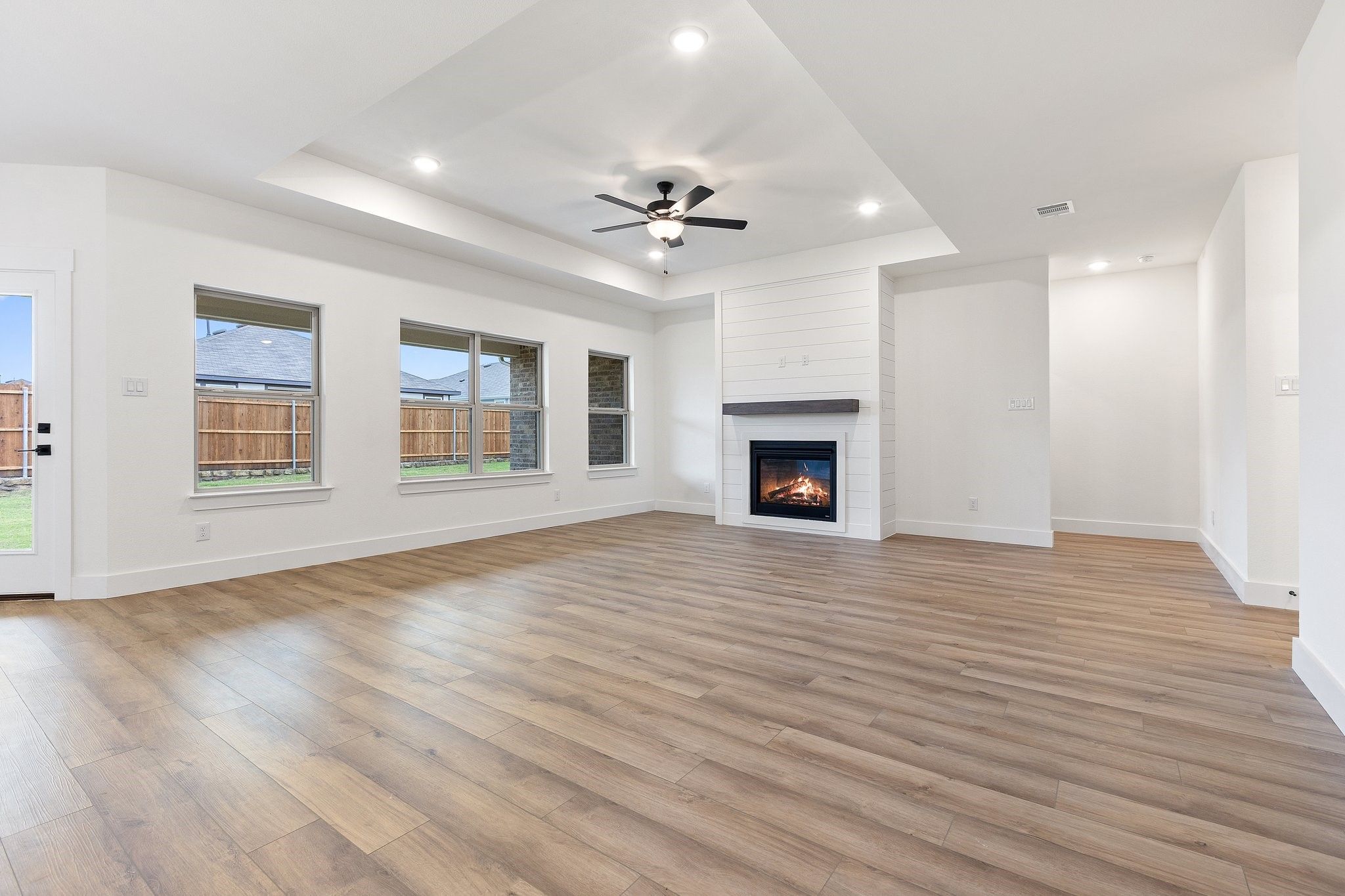 Bright open living room with tray ceiling, fireplace, and wood-look floors in The Rockford C home in Josephine, Texas.