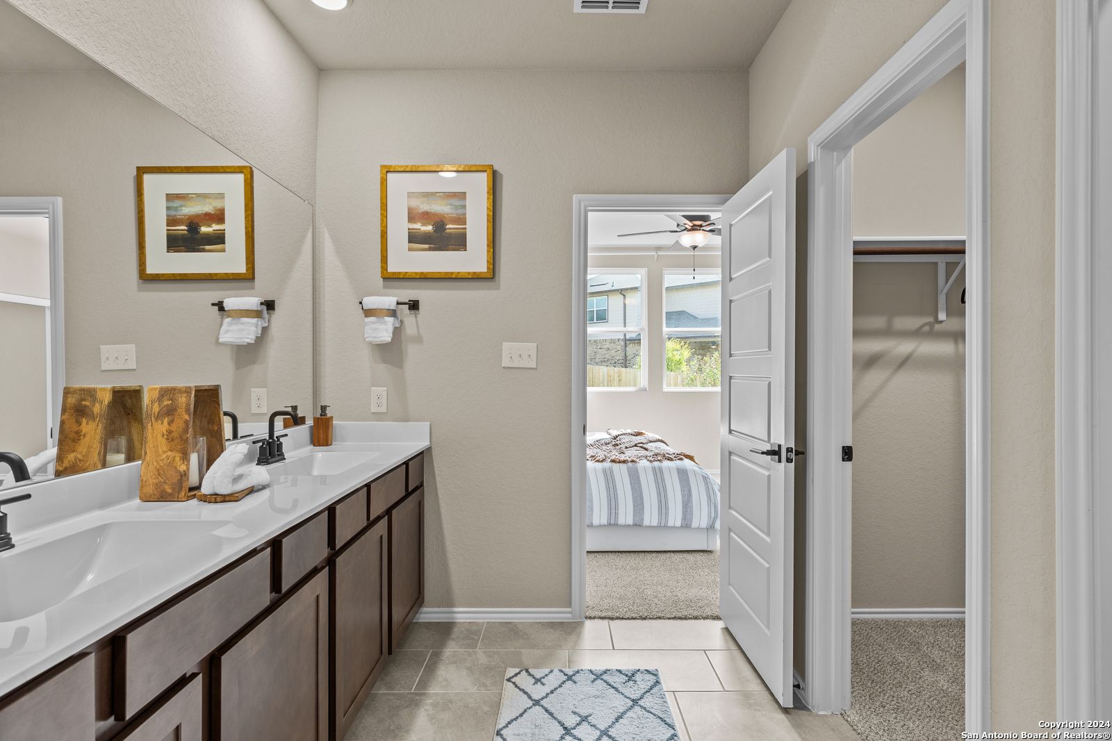 Elegant master bathroom featuring double vanity, mirrors, and open door to bedroom in Davidson Homes The Douglas F, Bricewood, San Antonio