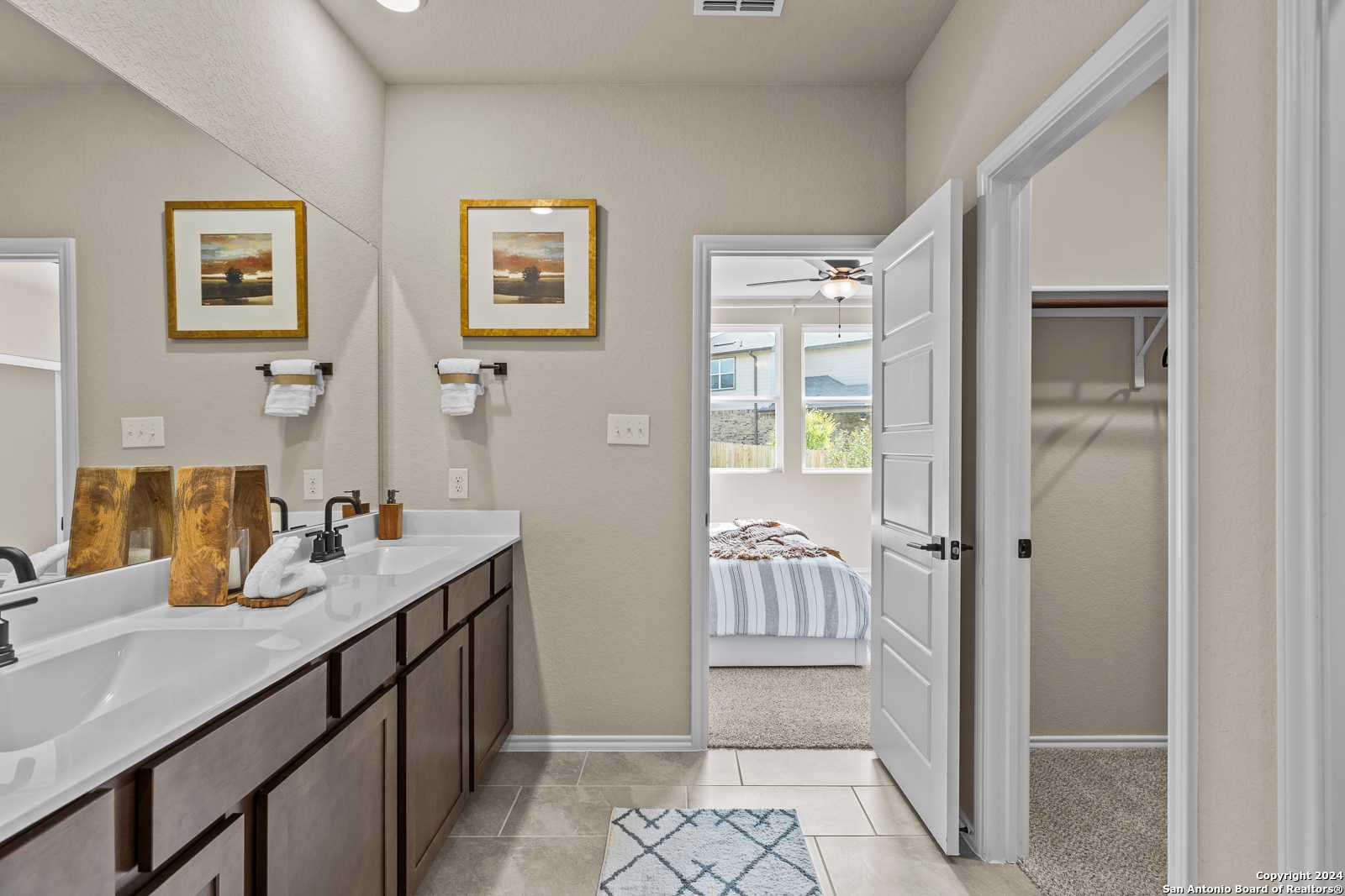 Elegant master bathroom featuring double vanity, mirrors, and open door to bedroom in Davidson Homes The Douglas F, Bricewood, San Antonio