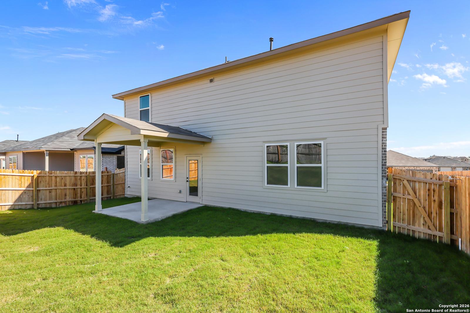 Two-story beige home exterior with covered side porch, double windows, and lush green yard in Comanche Ridge, San Antonio